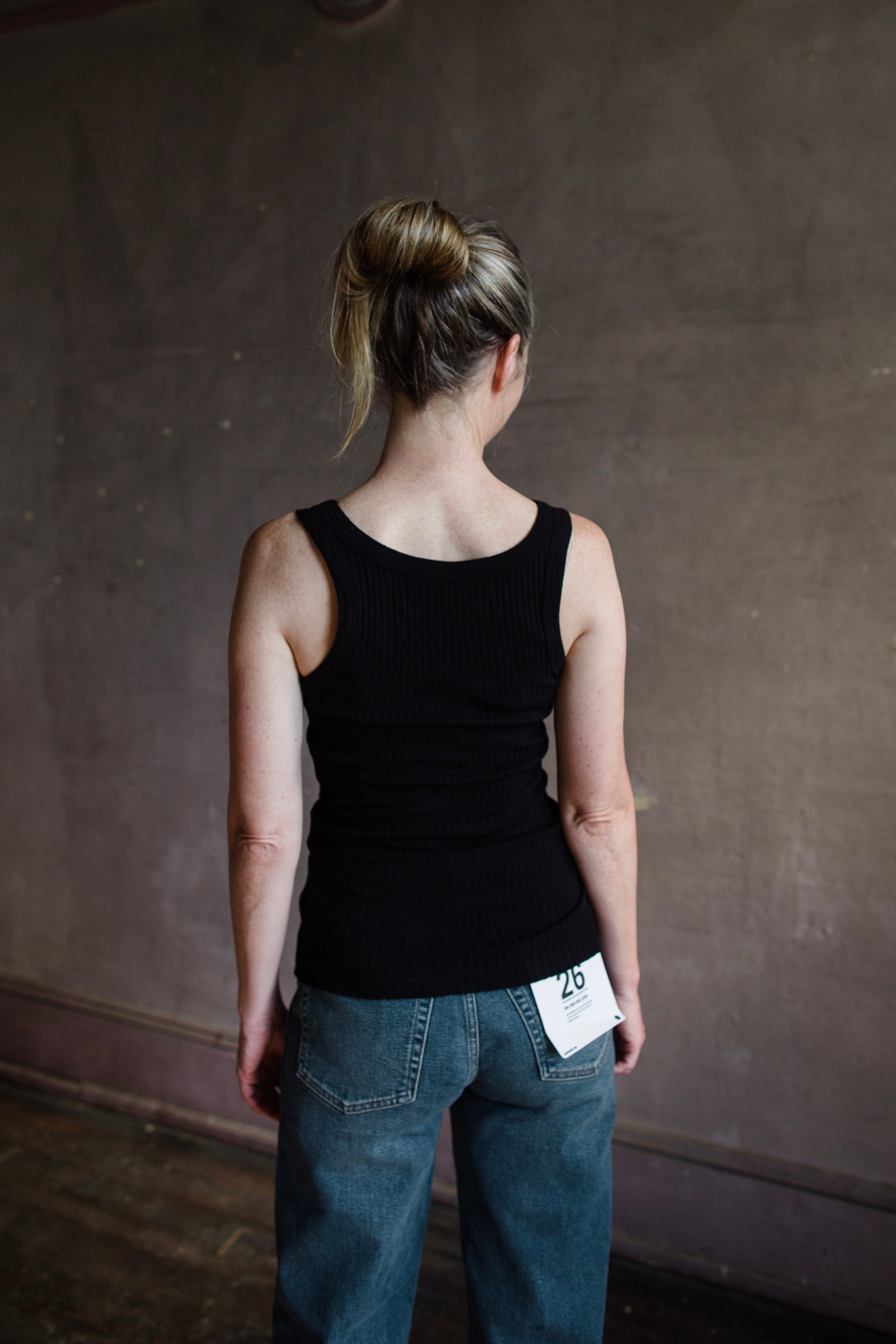 Image featuring a woman wearing the organic cotton tank top by Enza Costa is crafted from sweater rib material with a feminine U-neckline and a tubular finish in black.