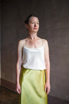 Image featuring a woman wearing the white Silk Satin Camisole from Enza Costa with a feminine scoop neckline, delicate straps, a gently flared hem and relaxed fit.