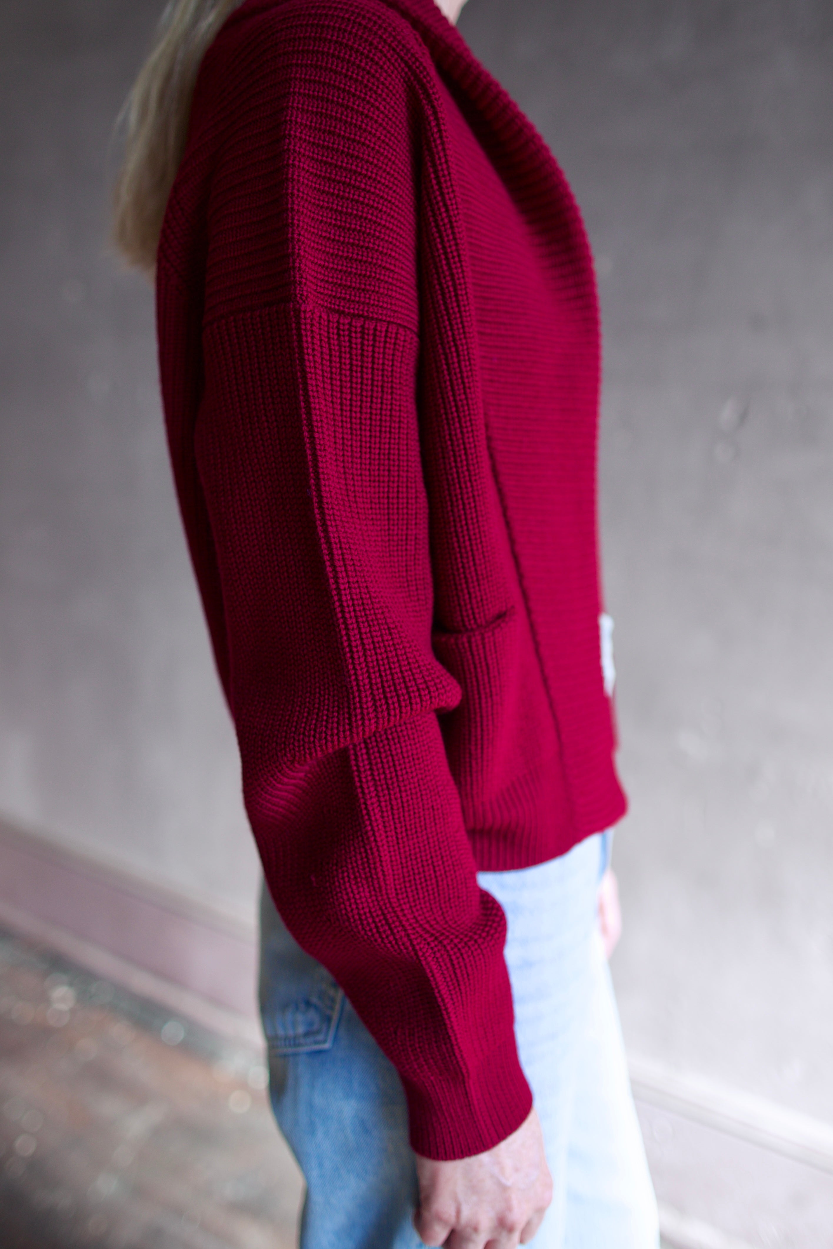 Model wearing a ruby red Forte Forte Merinos cardigan featuring a shawl wrap collar and long sleeves in vrigin wool