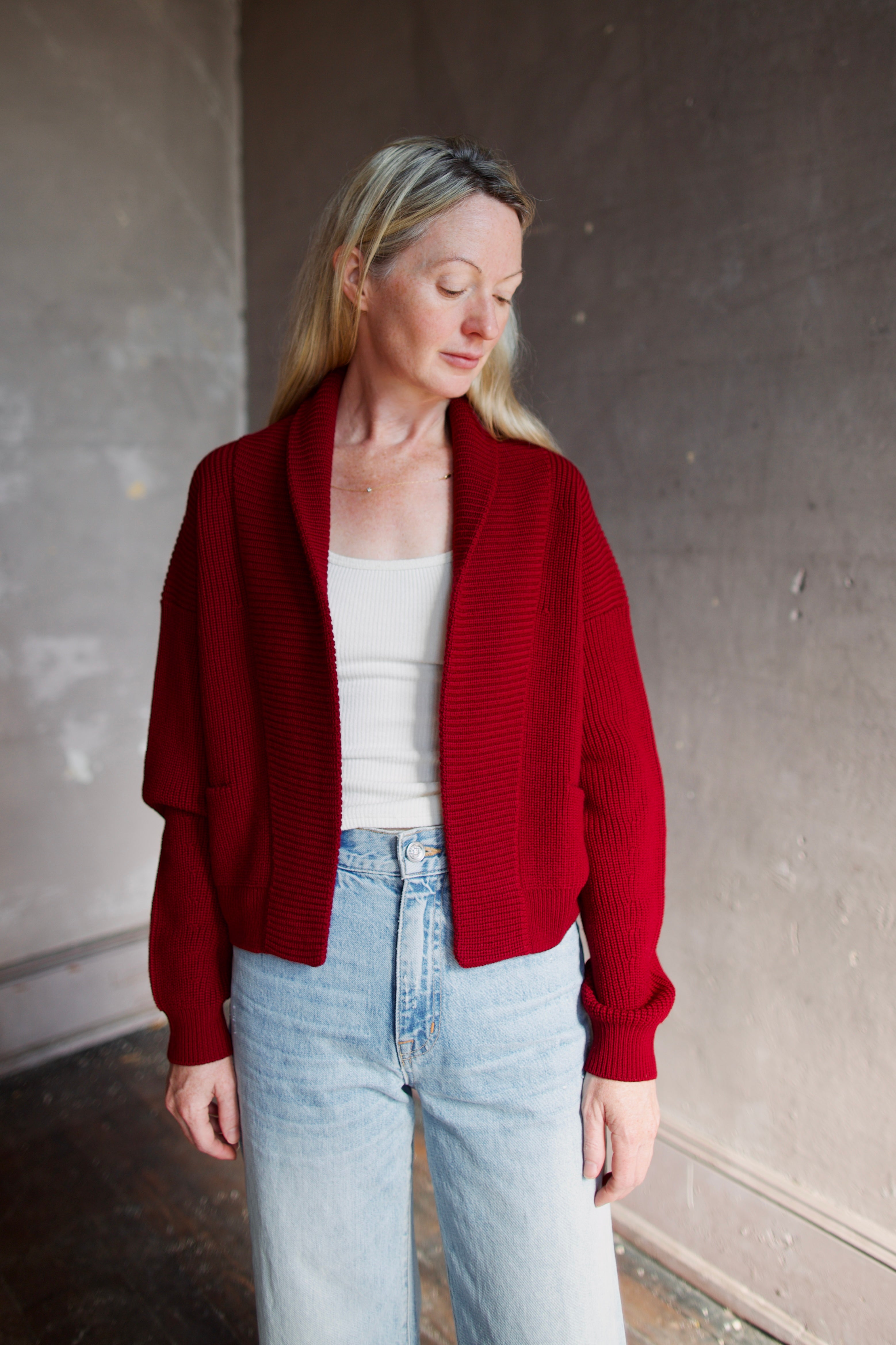 Model wearing a ruby red Forte Forte Merinos cardigan featuring a shawl wrap collar and long sleeves in vrigin wool
