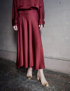 Image featuring a woman wearing a burgundy silk satin skirt by Forte Forte with a high rise, slim fit with slightly flared skirting.