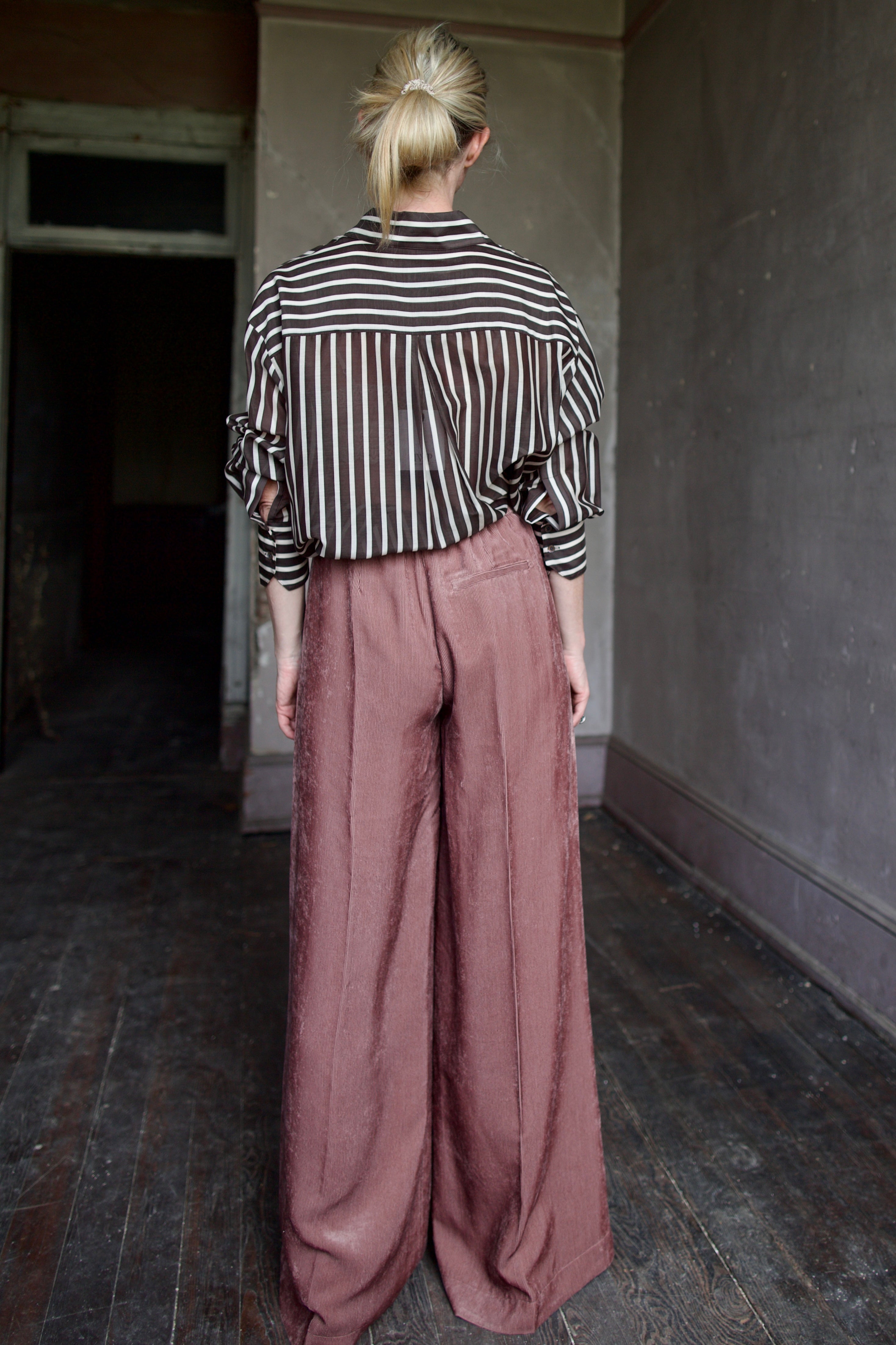 Back image of mature model wearing luxury designer Forte Forte mauve velvet corduroy pleated front pant and TWP brown and cream striped button down shirt