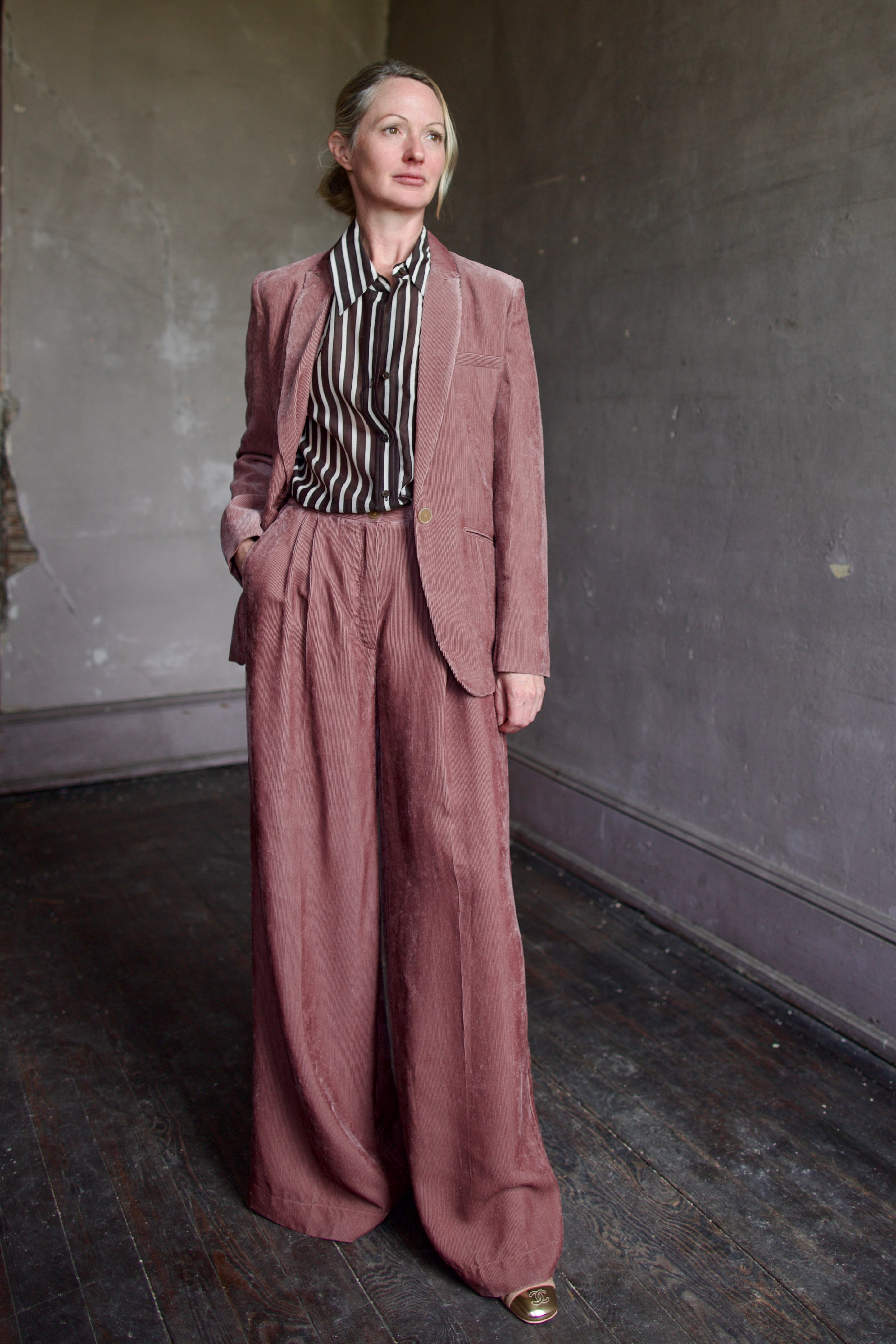 Mature model wearing luxury designers Forte Forte mauve velvet corduroy pleated front pant and TWP silk cotton striped button down shirt