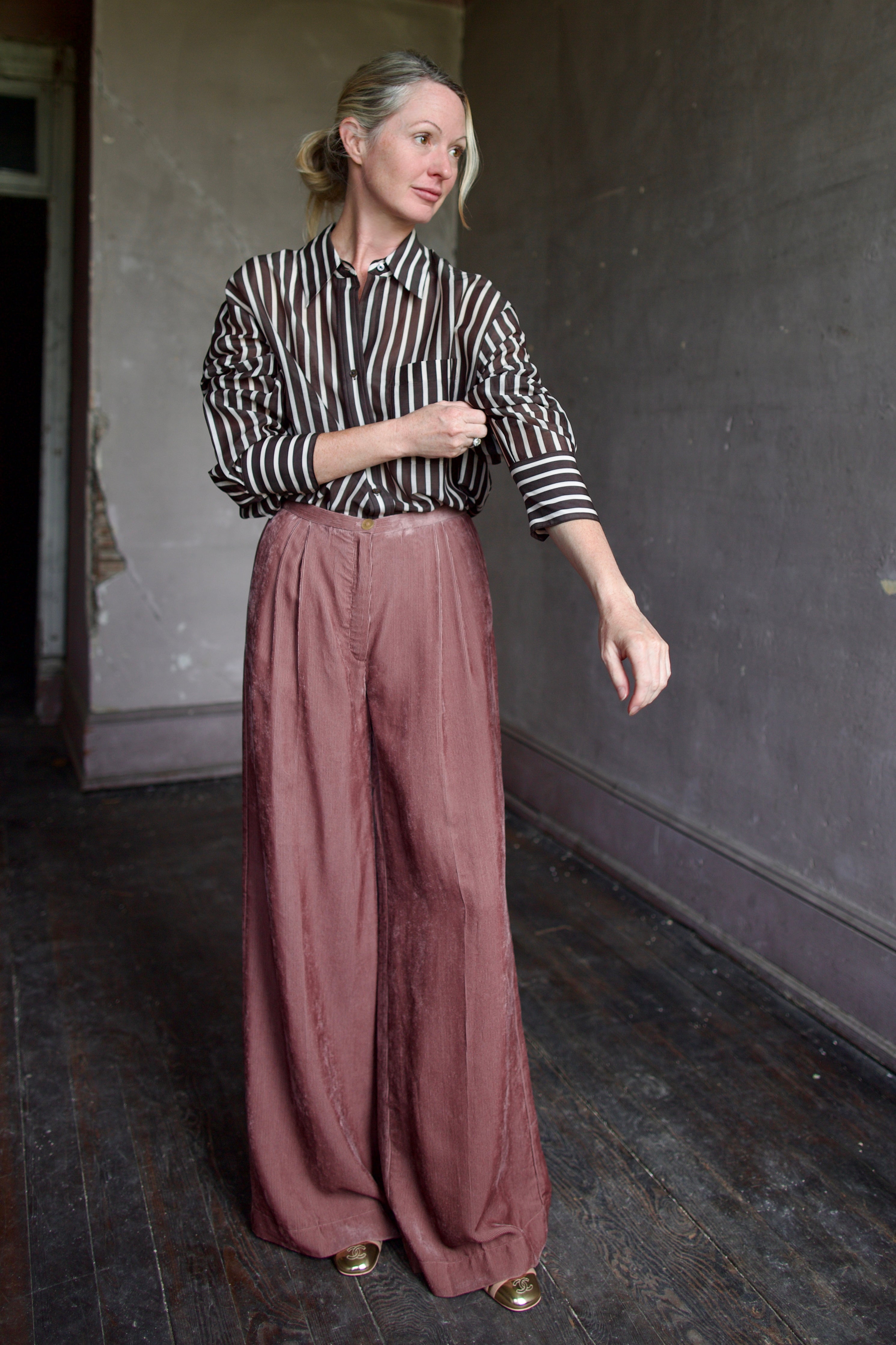 Image of mature model wearing luxury designers Forte Forte mauve velvet corduroy pleated front pant and TWP brown and cream striped button down shirt