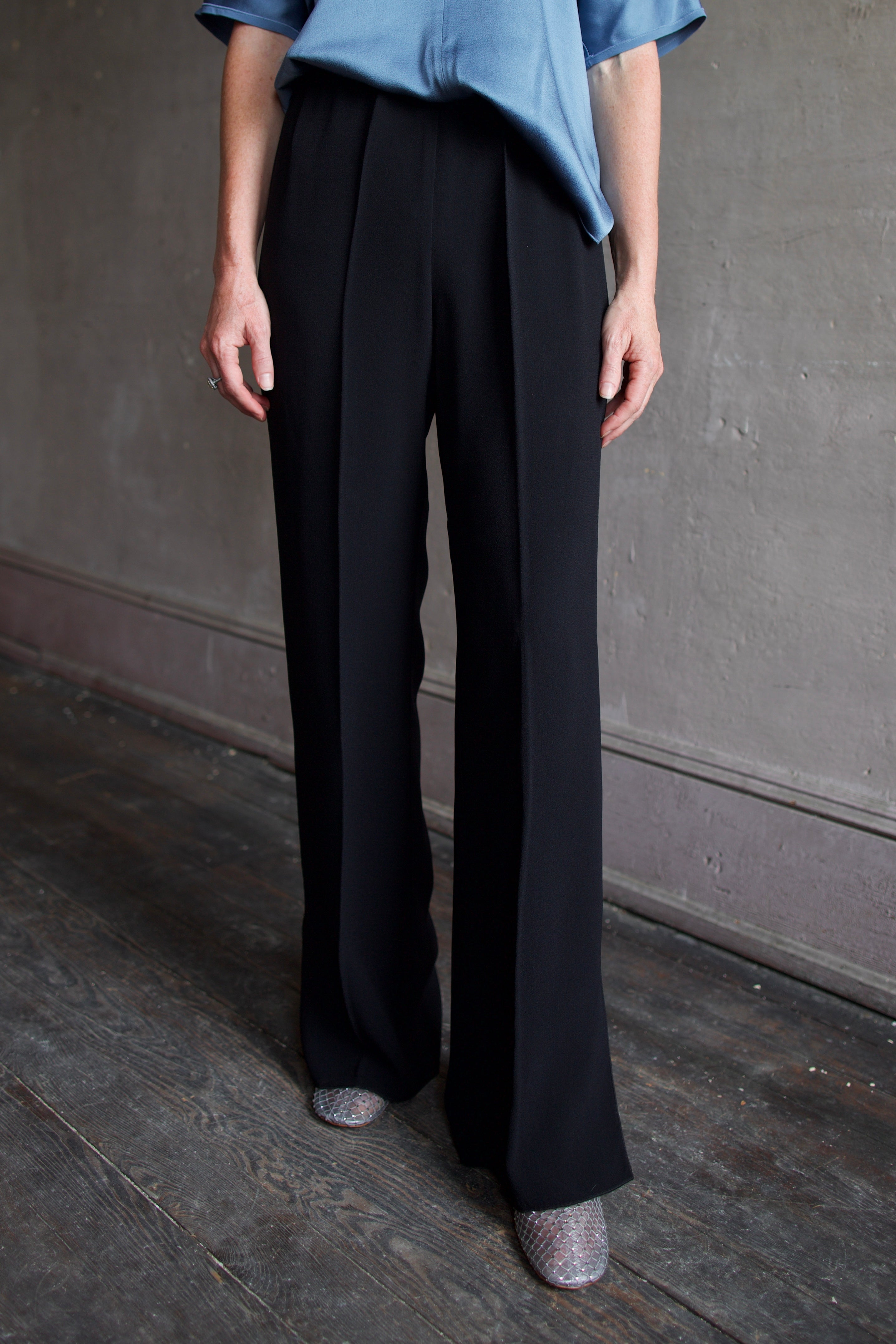 Mature model wearing luxury Italian designer black wide-leg pants, a blue shirt and crystal boots by Forte Forte