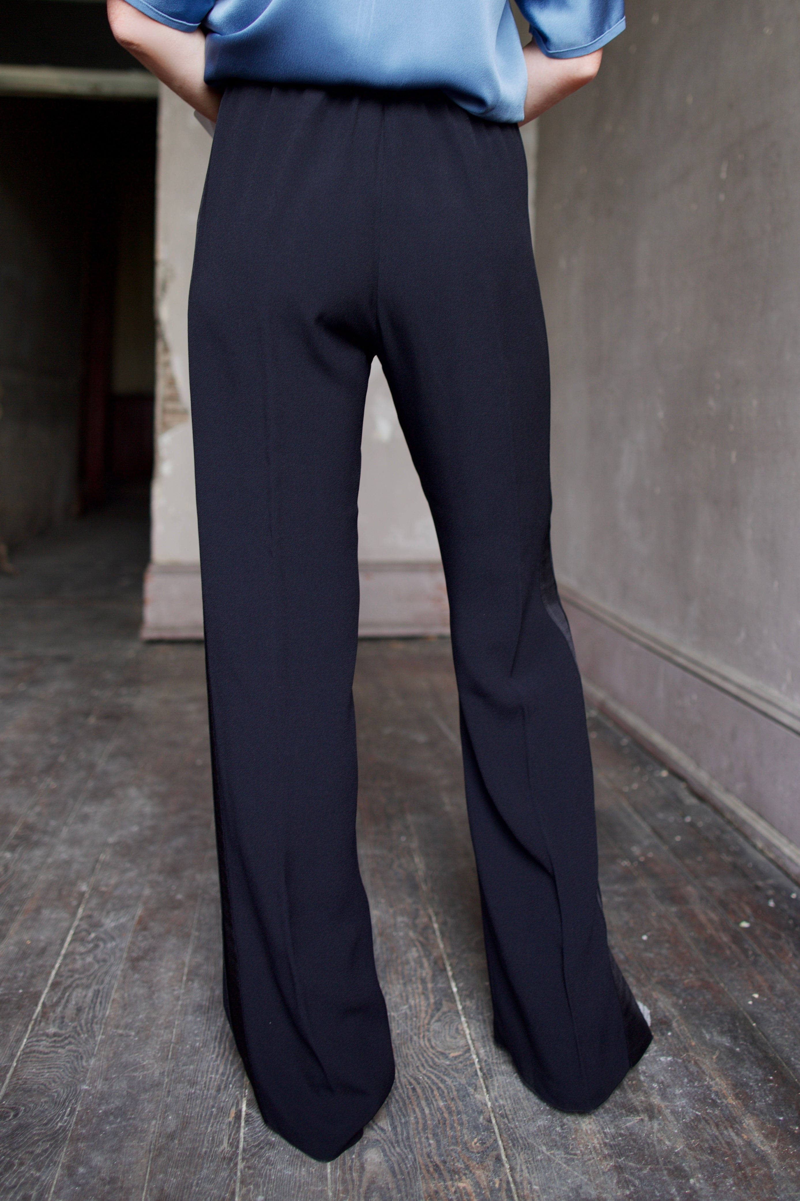 Back of mature model wearing luxury Italian designer black wide-leg pants, a blue shirt and crystal boots by Forte Forte