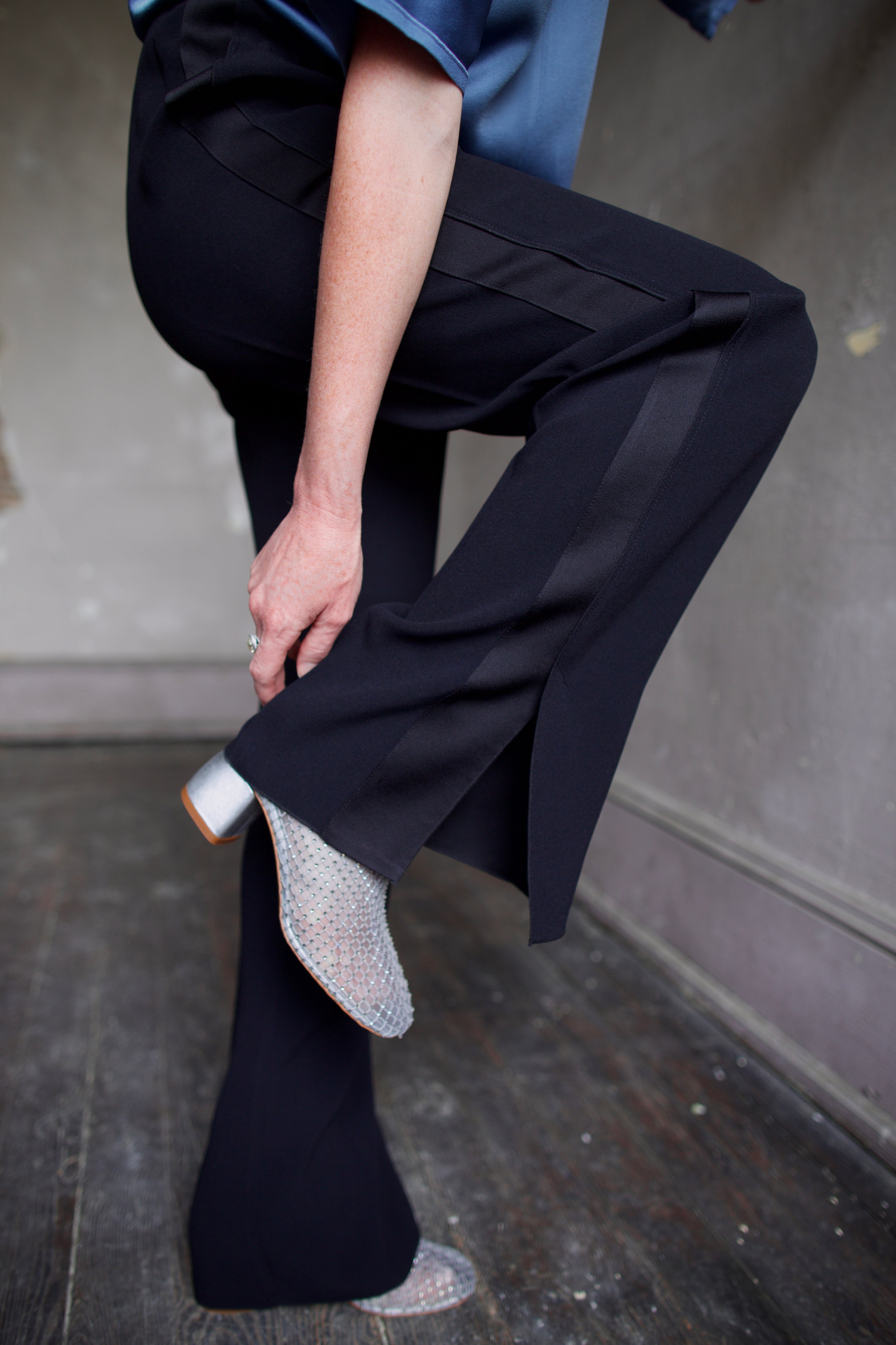 Mature model wearing luxury Italian designer black pants with tuxedo stripe, a blue shirt and crystal boots by Forte Forte