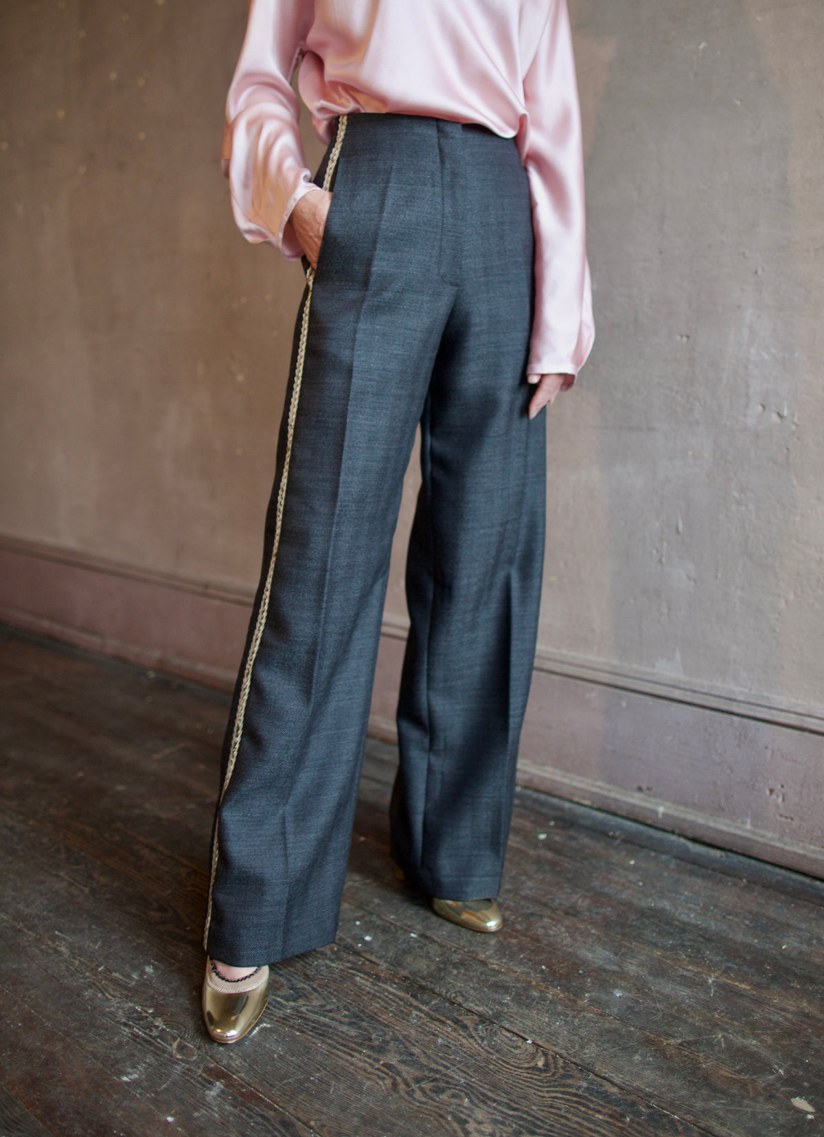 Mature woman wearing Forte_Forte's tailored Grey Herringbone Pants in virgin wool asymmetrical sequence embellishment down side