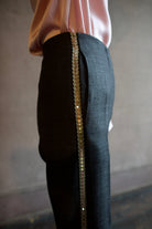 Mature woman wearing Forte_Forte's tailored Grey Herringbone Pants in virgin wool asymmetrical sequence embellishment down side