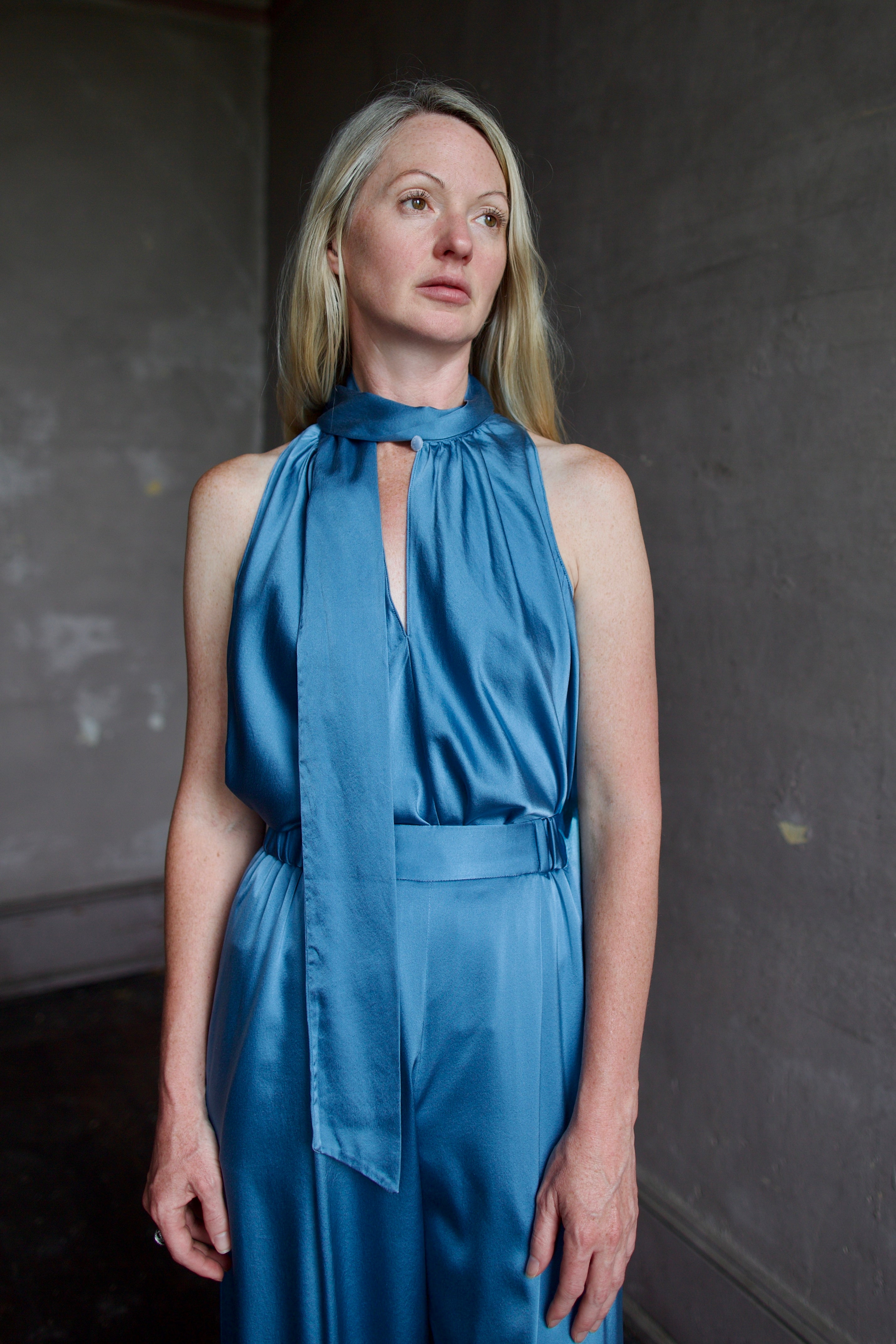 Model wearing high-end designer Forte Forte blue silk sleeveless top and pant set against a dark background