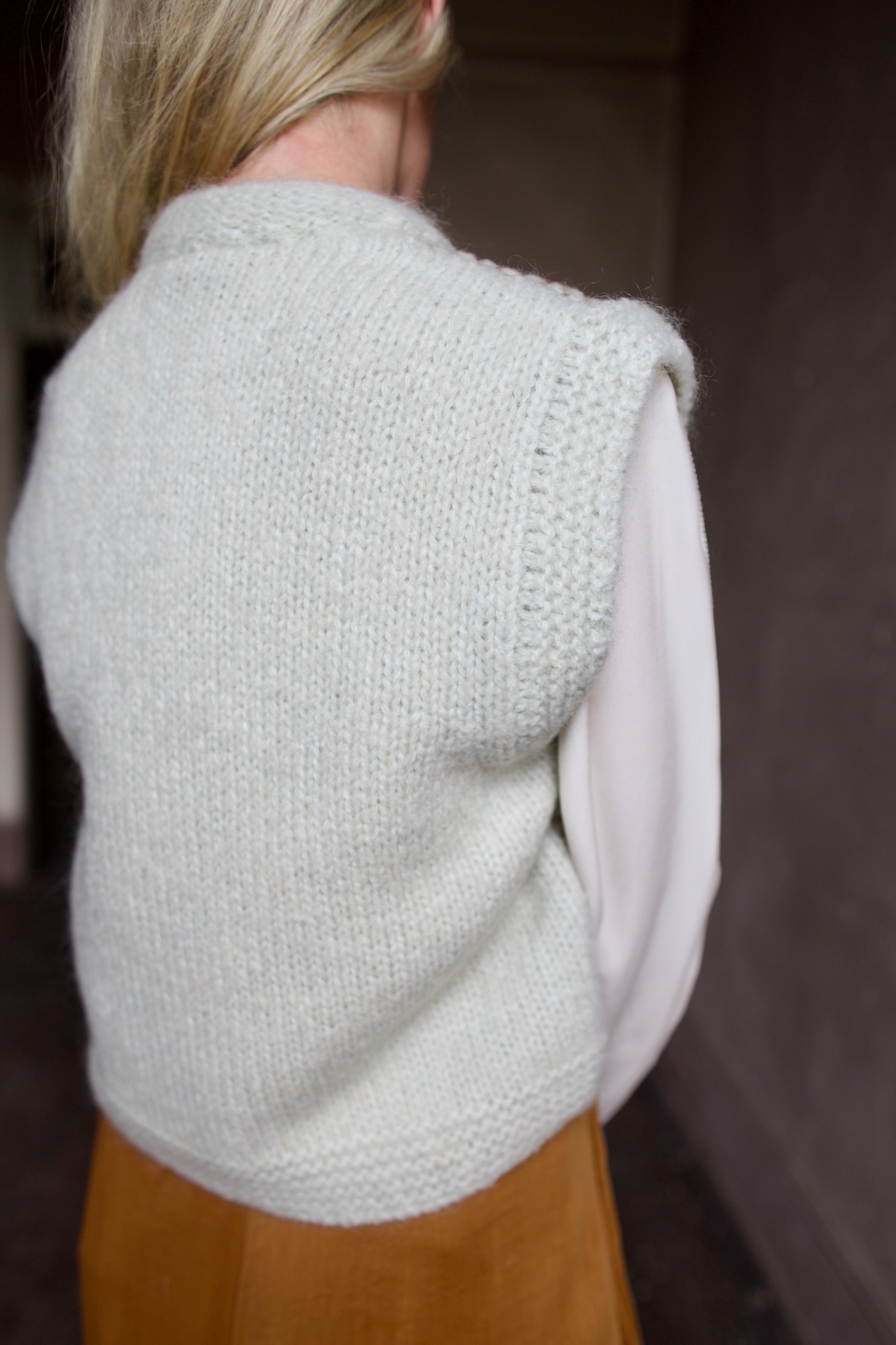 Back of mature model wearing designer clothing Ulla Johnson white blouse with Forte Forte  skirt and mint  green layering sweater vest 