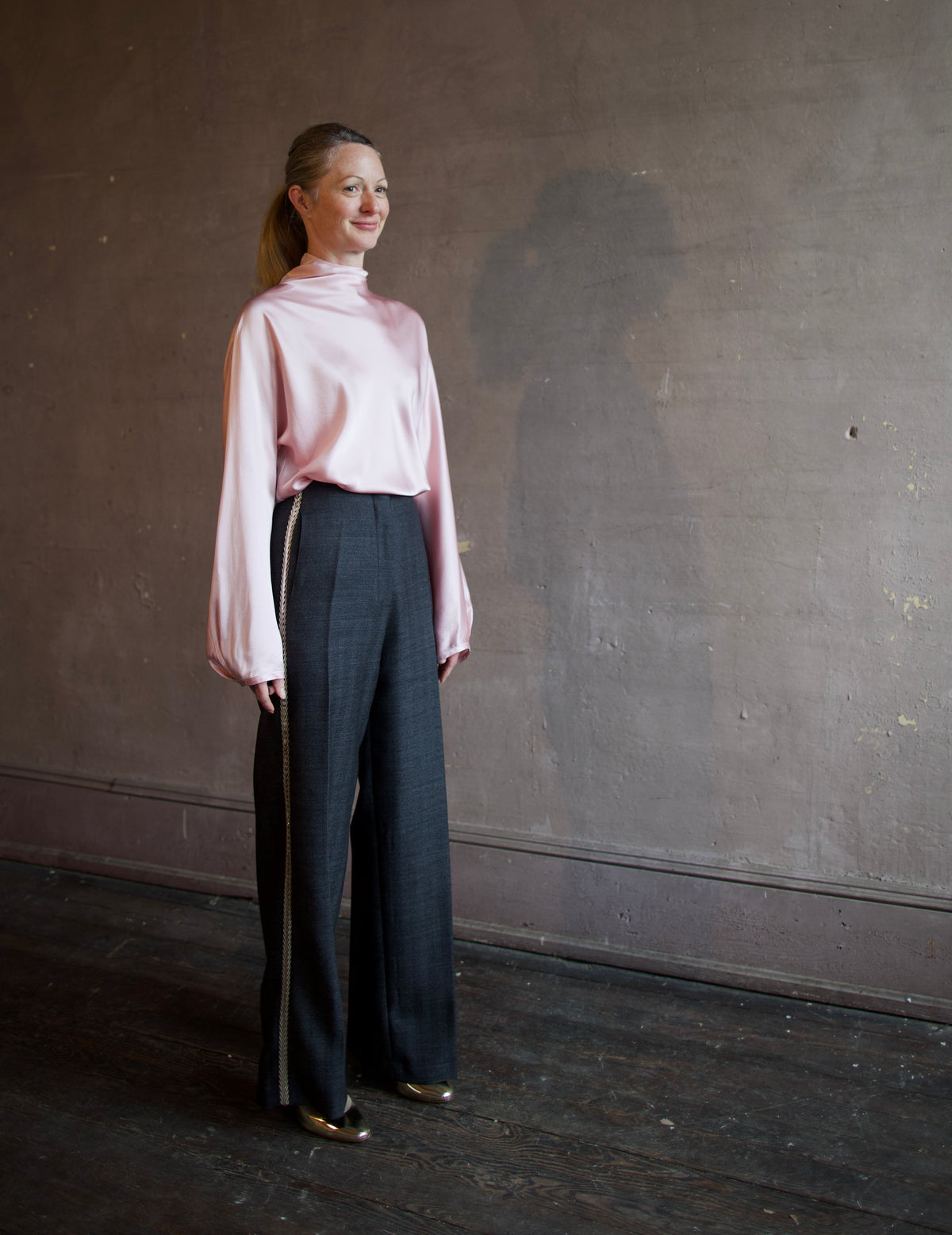 Mature woman wearing Forte_Forte's tailored Grey Herringbone Pants in virgin wool asymmetrical sequence embellishment down side