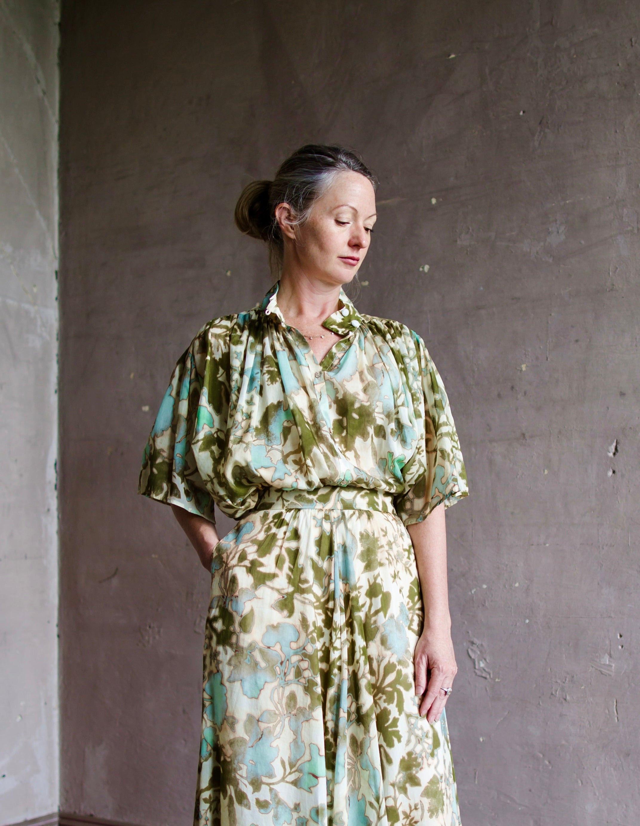 Image of a woman wearing the bloom mist top by Forte Forte features a stand up collar with short sleeves and pleating in a cotton silk green floral print.