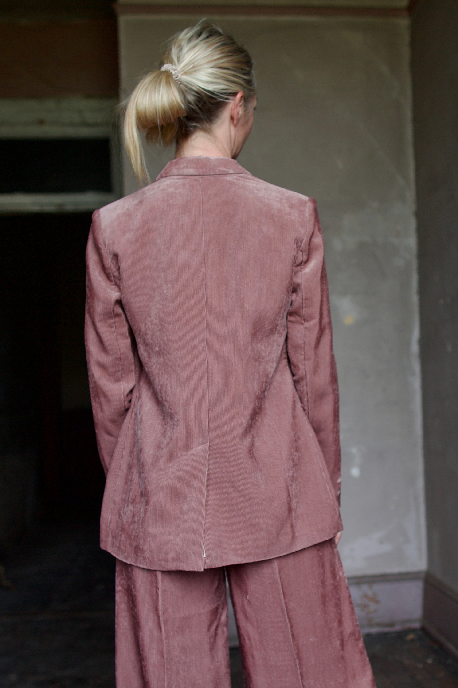Back of a mature model wearing luxury Italian designer Forte Forte mauve velvet corduroy jacket and pant set 