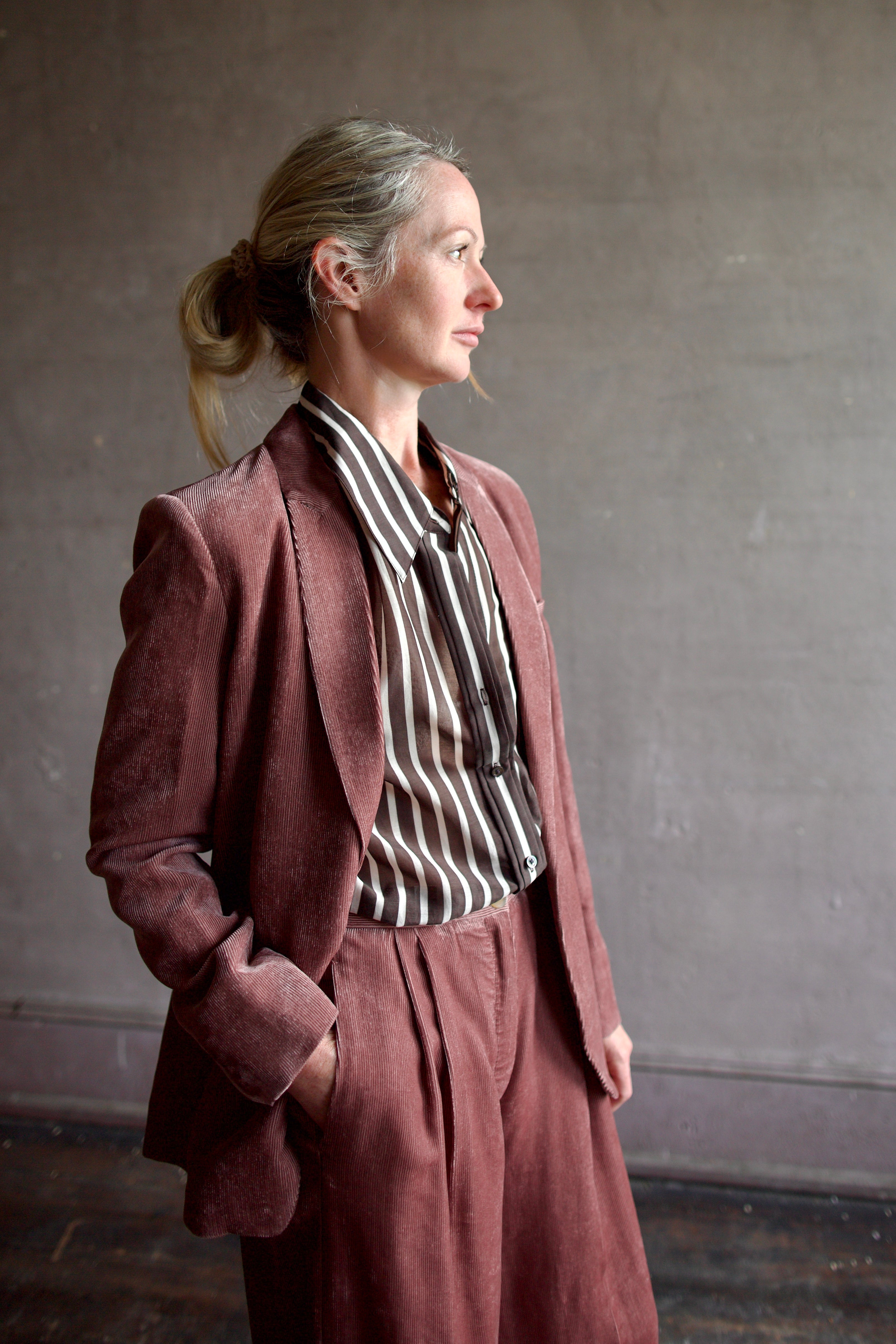 Image of mature model wearing luxury designer Forte Forte mauve velvet corduroy pleated front pant and TWP brown and cream striped button down shirt