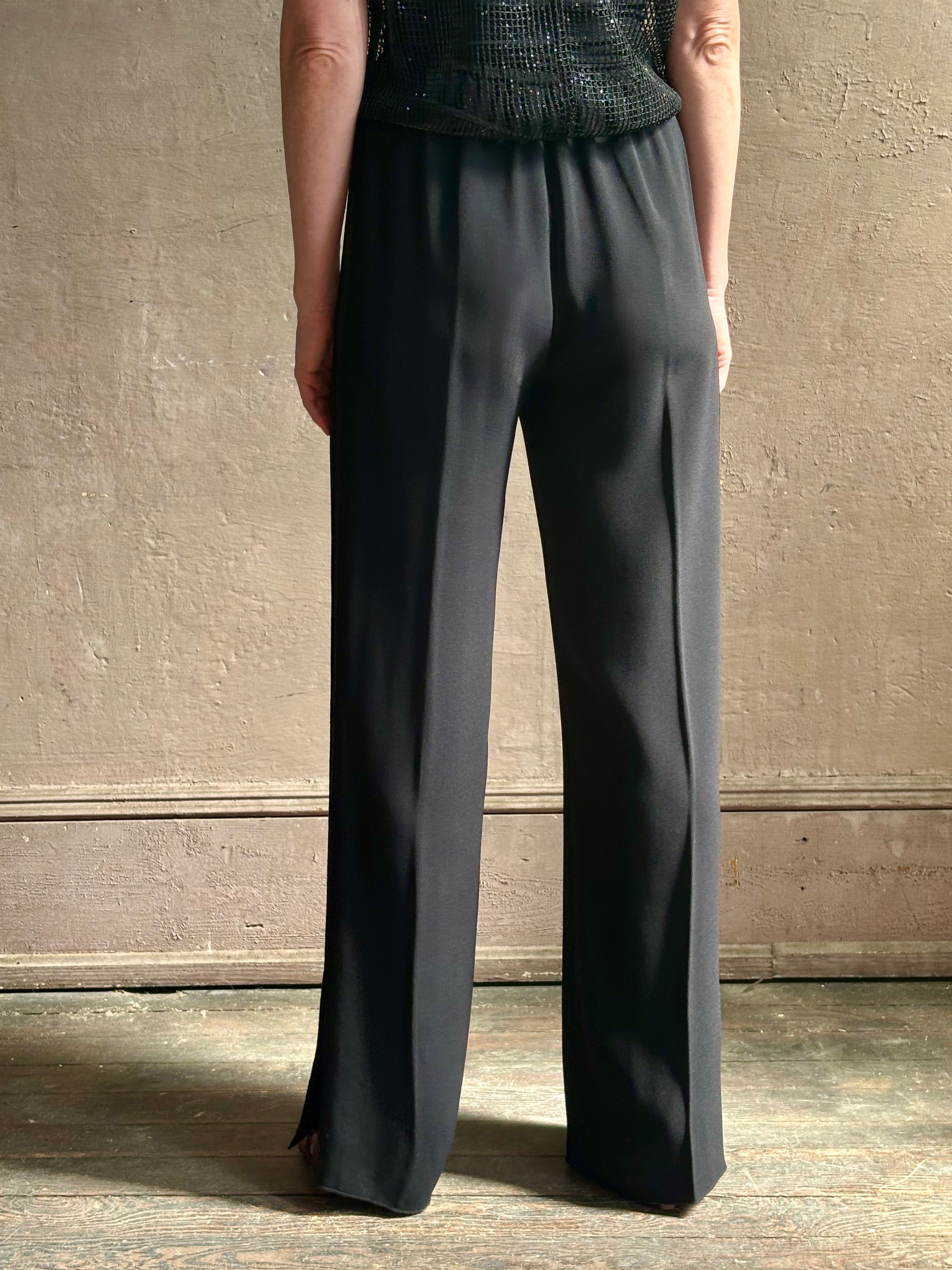 Mature model wearing luxury Italian designer Forte Forte black wide-leg pull on pants with satin tuxedo side stripe and bottom slit