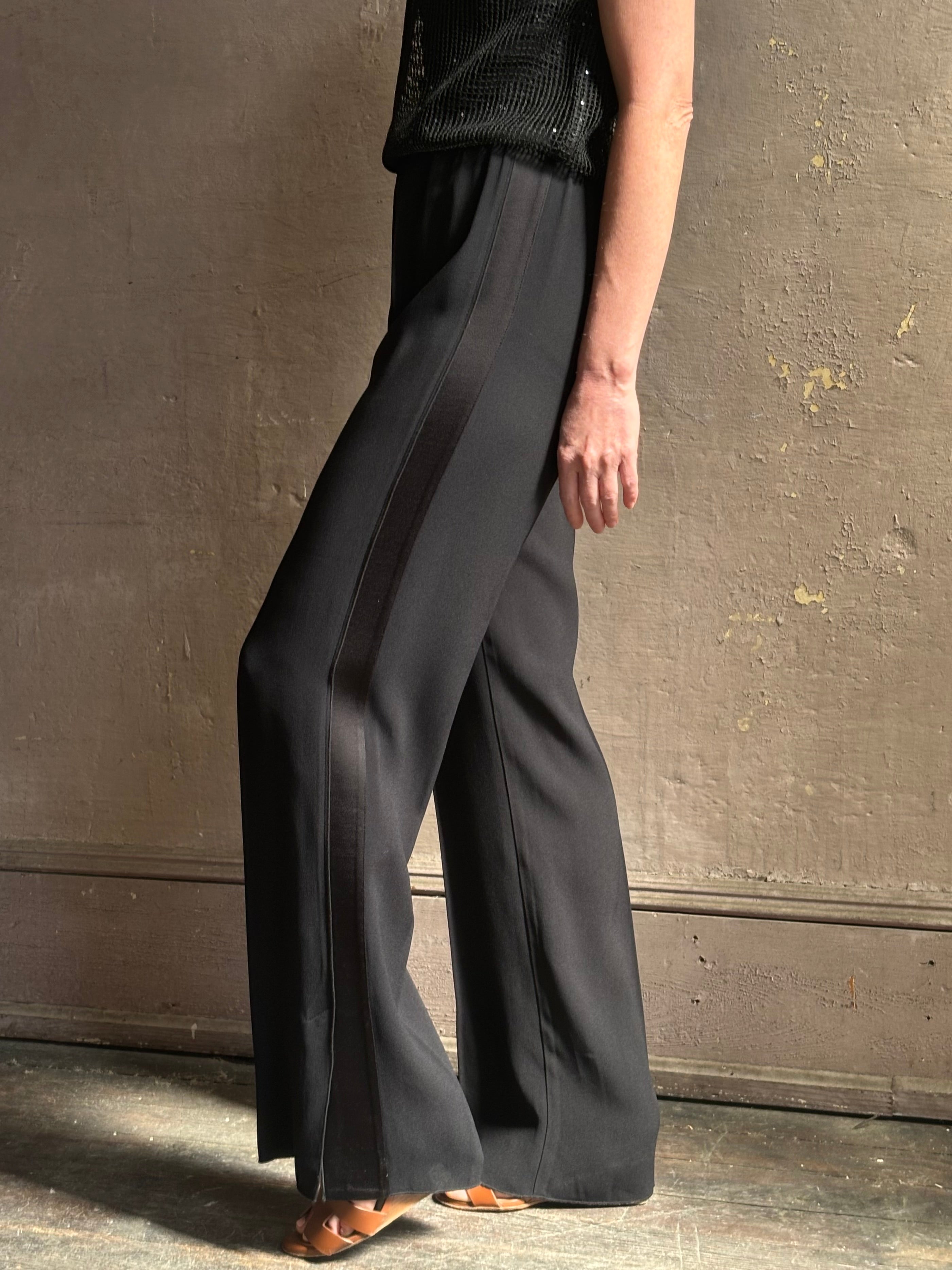 Mature model wearing luxury Italian designer Forte Forte black wide-leg pull on pants with satin tuxedo side stripe and bottom slit