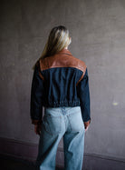 Image featuring a woman wearing the Atelier cropped denim jacket by Frame with a button front, tailored fit and brown leather trim.