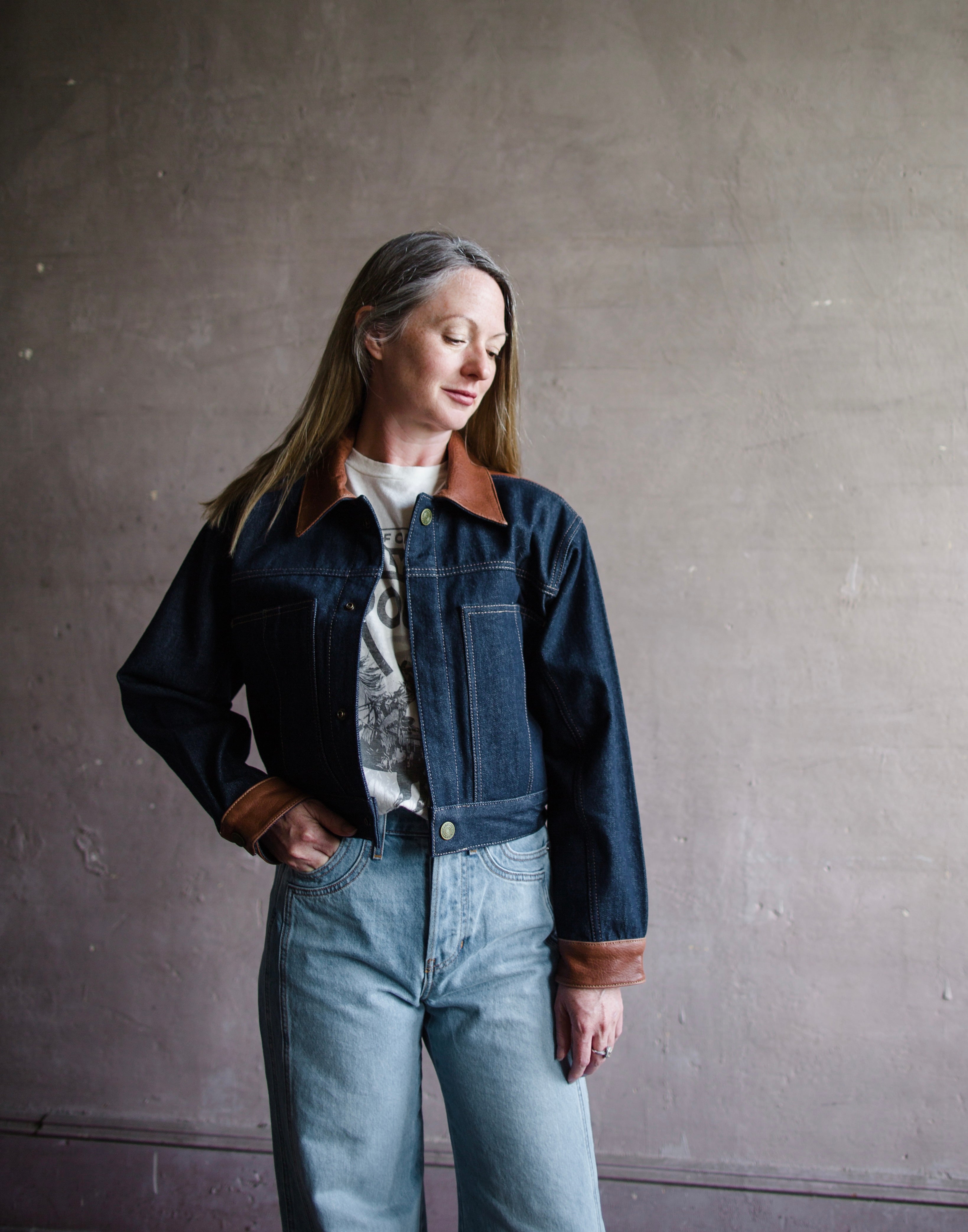 Image featuring a woman wearing the Atelier cropped denim jacket by Frame with a button front, tailored fit and brown leather trim.