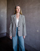 Image featuring a woman wearing the Frame Femme Blazer in hounds tooth wool with two-button long sleeve jacket, notch lapels, chest and side pockets.