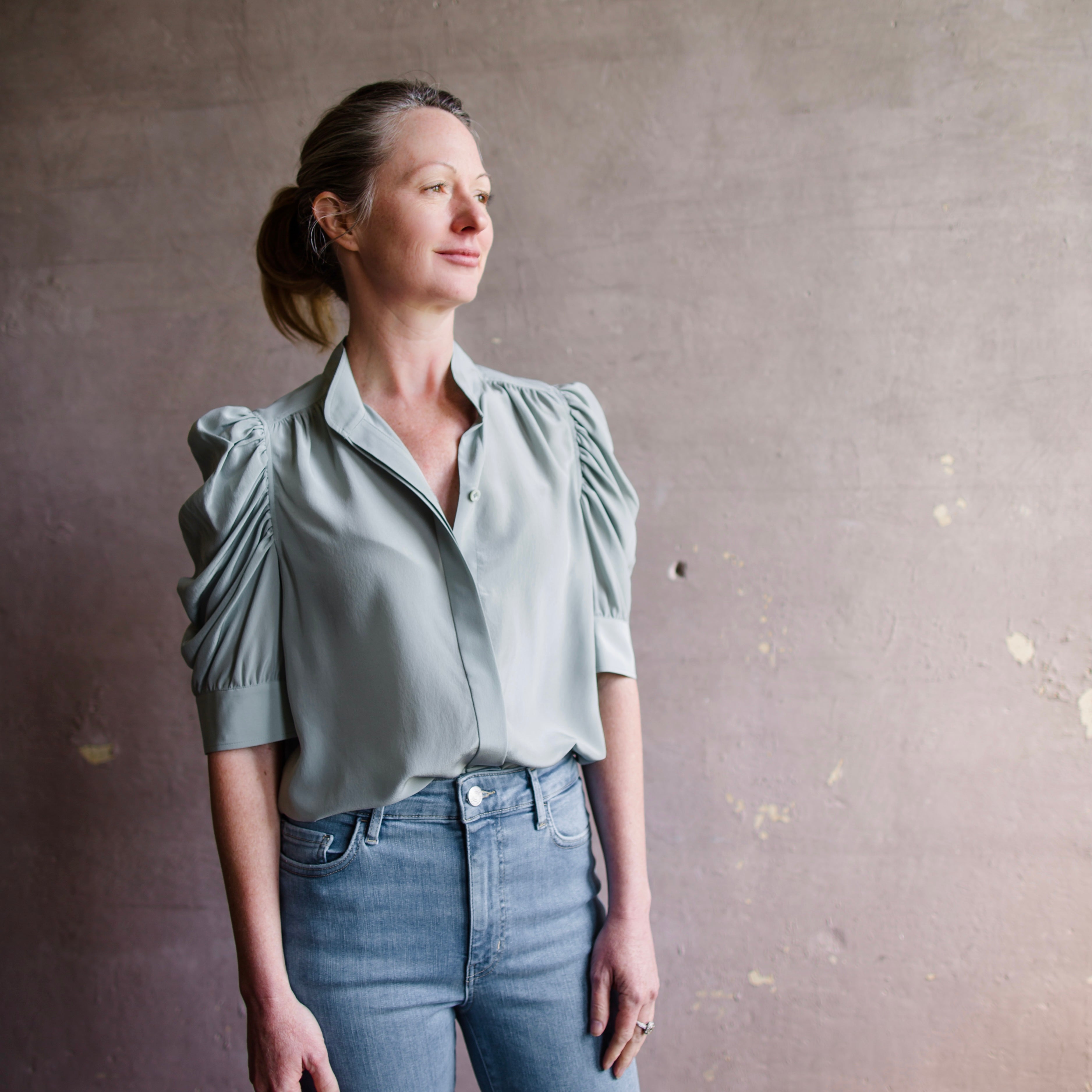 Image featuring a woman wearing the Frame gillian silk blouse with a high neckline and boldly puffed sleeves  in Sage Green.