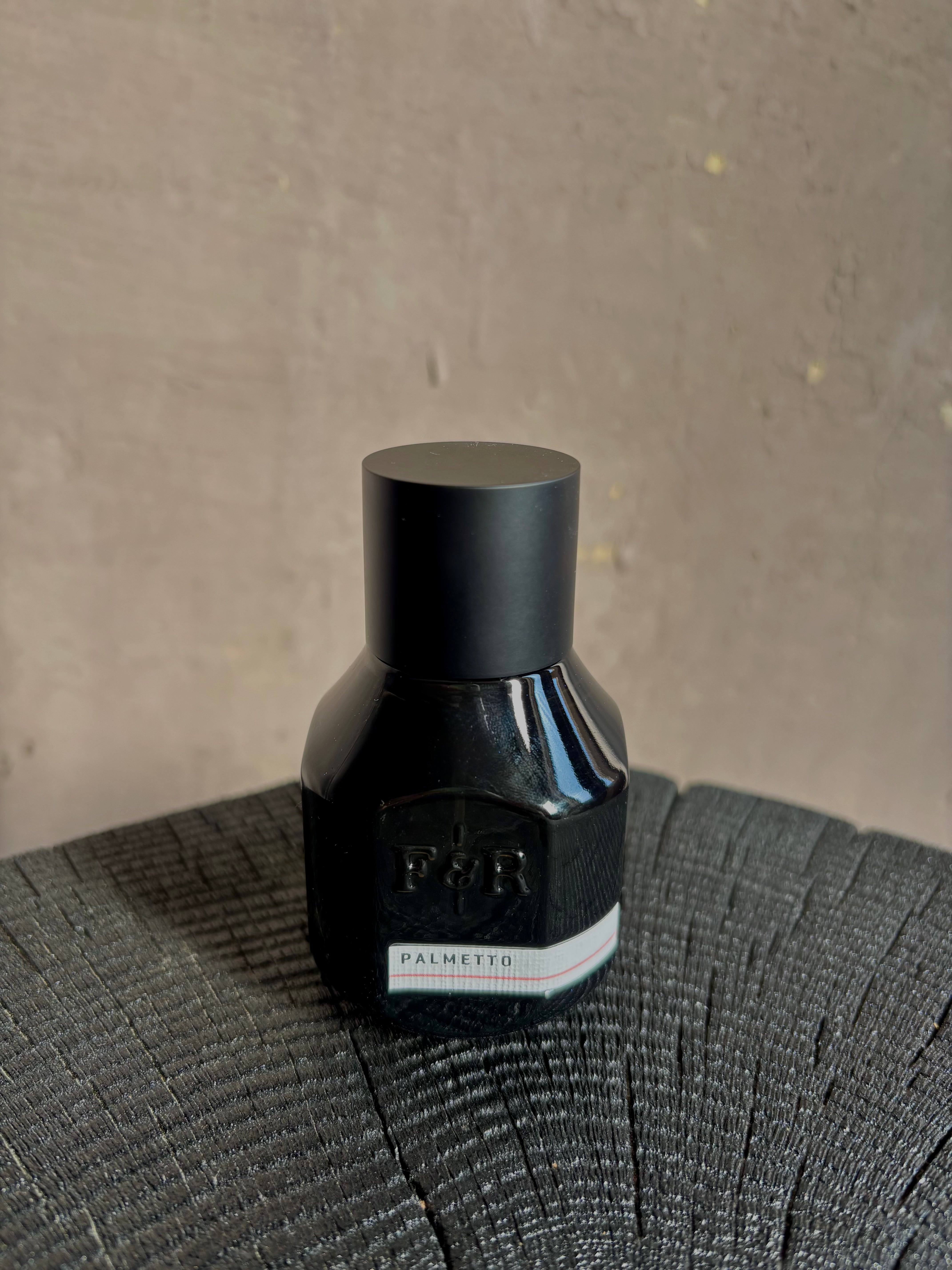 Image of  small black bottle with a matte black metal cap and a white label reading PALMETTO and F&R Monogramed Extrait de Parfum made in USA