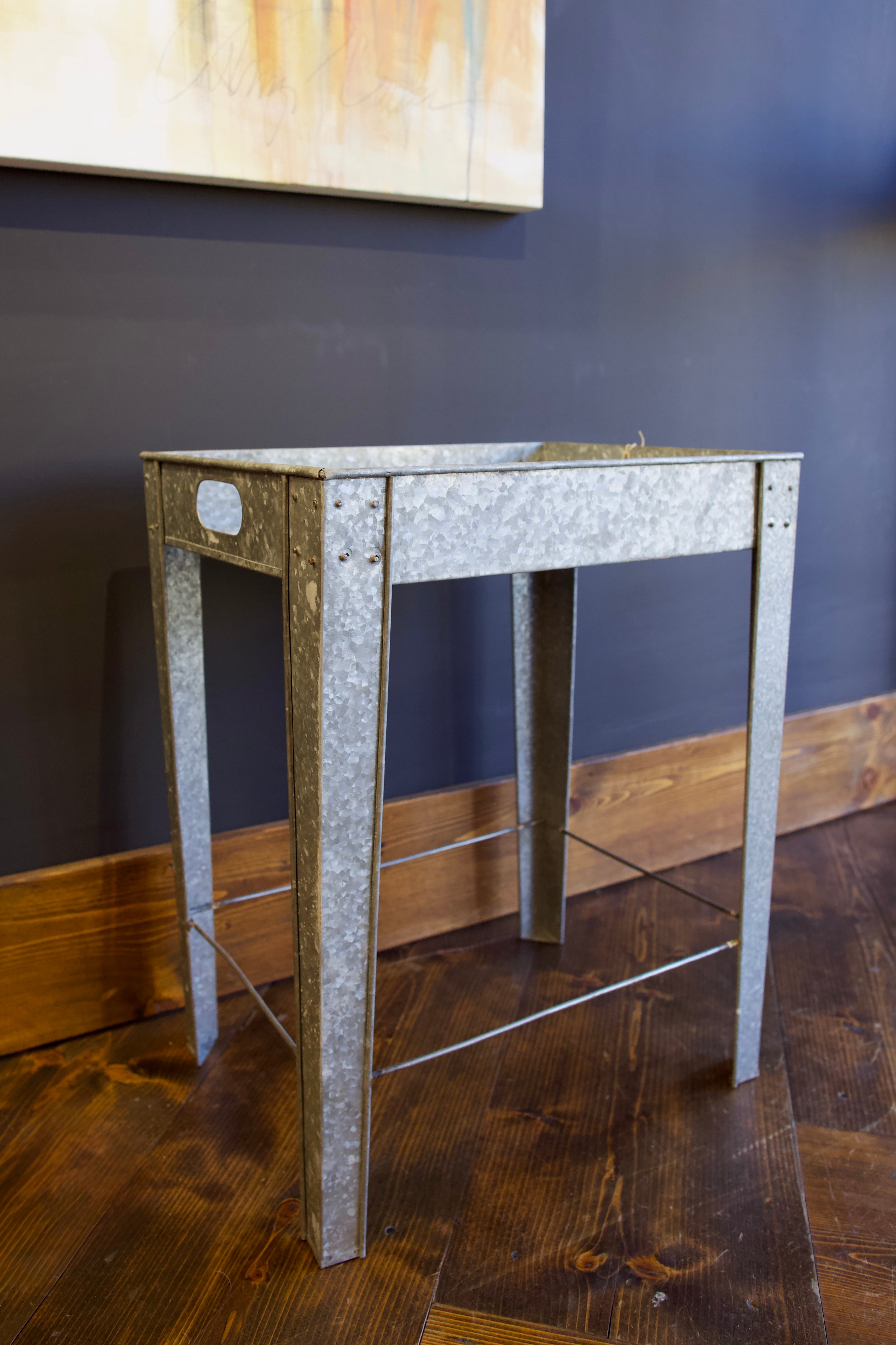 A rectangular galvanized metal tray table with side handles for indoor or outdoor versatility