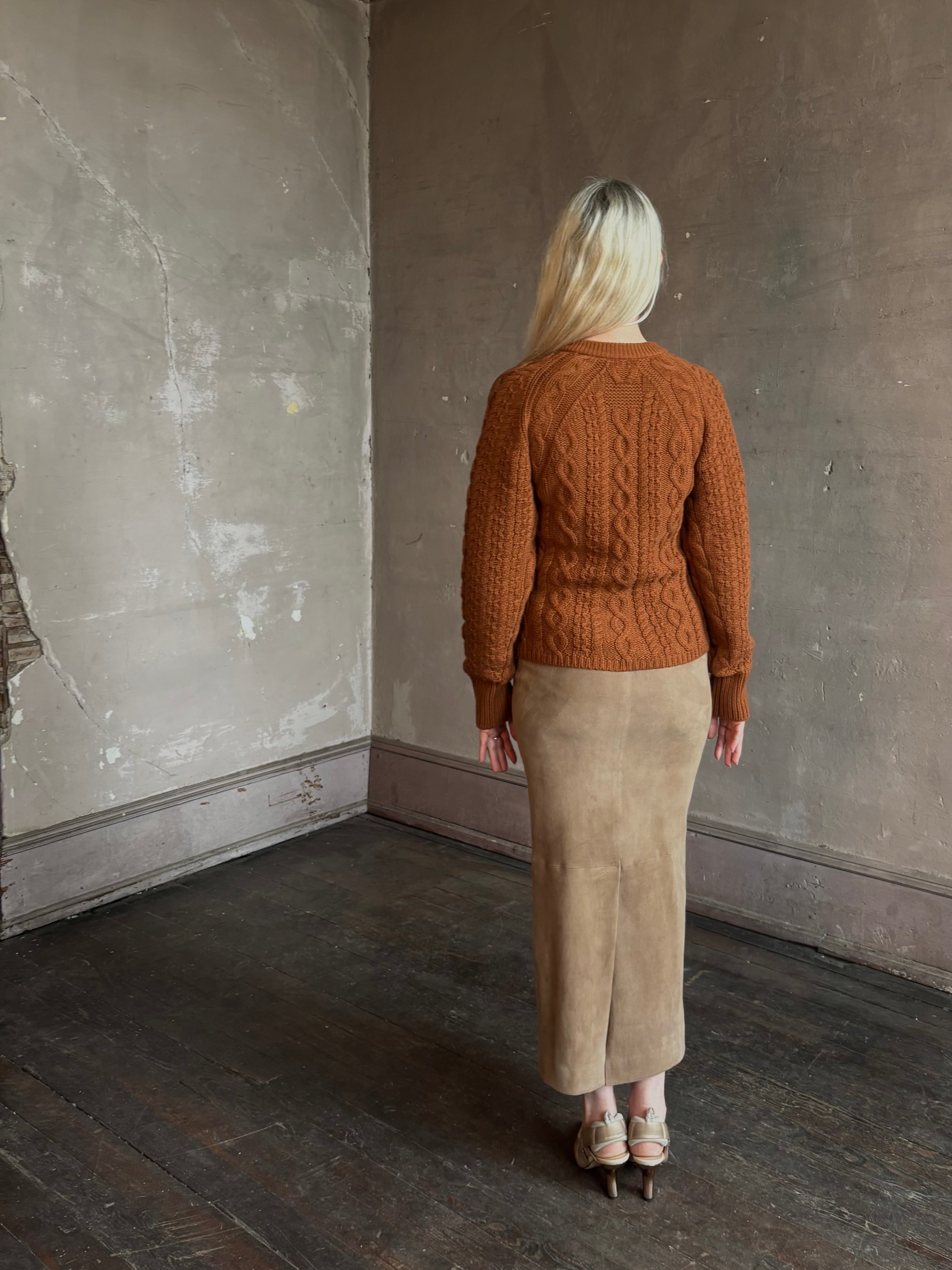 Mature woman wearing Guest in Residence's Cable Sculpted Cardigan Burnt Sienna wool-cashmere cable knit raglan sleeves. Richly textured heirloom-quality warmth