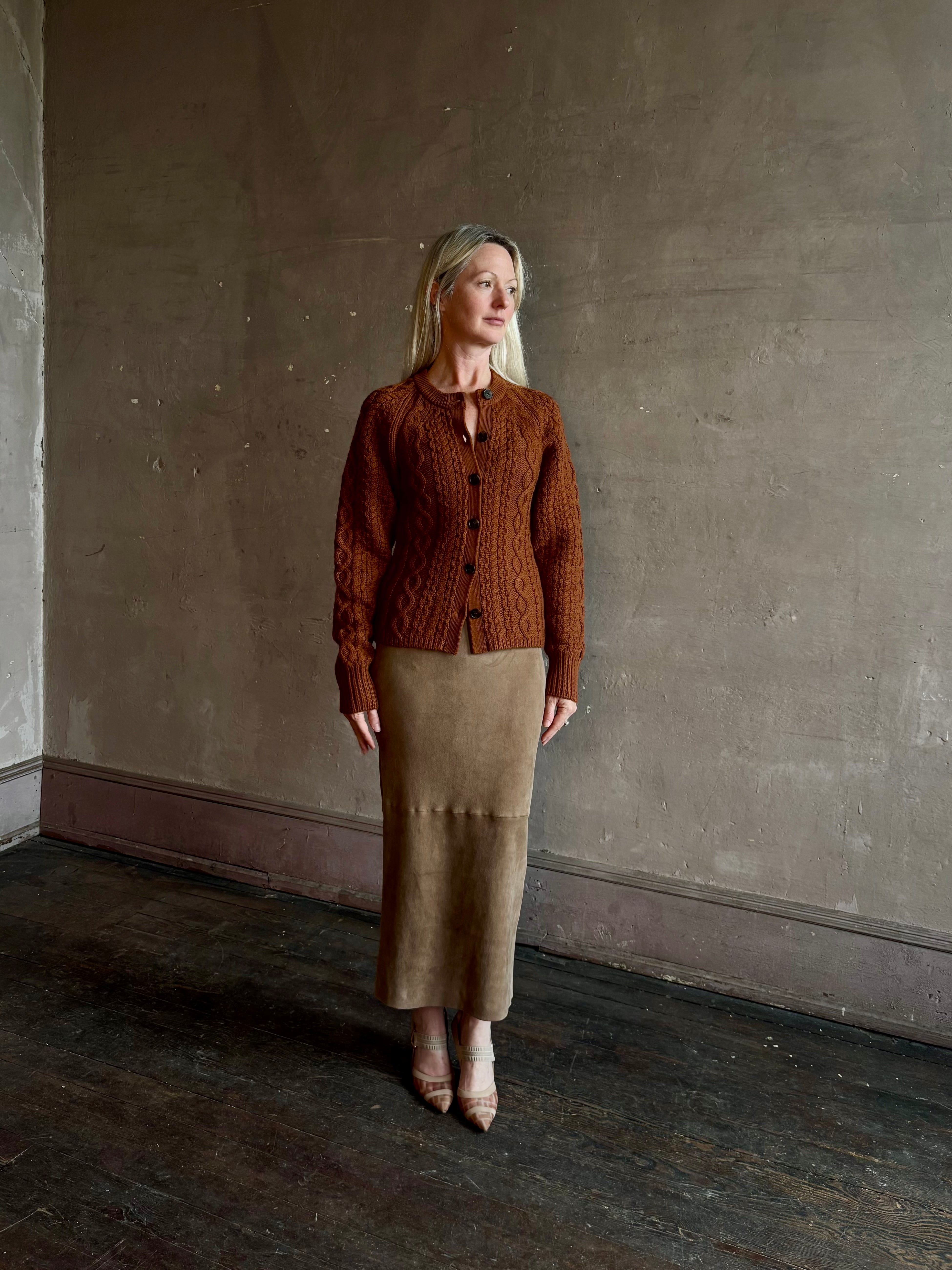Mature woman wearing Guest in Residence's Cable Sculpted Cardigan Burnt Sienna wool-cashmere cable knit raglan sleeves. Richly textured heirloom-quality warmth