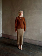 Mature woman wearing Guest in Residence's Cable Sculpted Cardigan Burnt Sienna wool-cashmere cable knit raglan sleeves. Richly textured heirloom-quality warmth