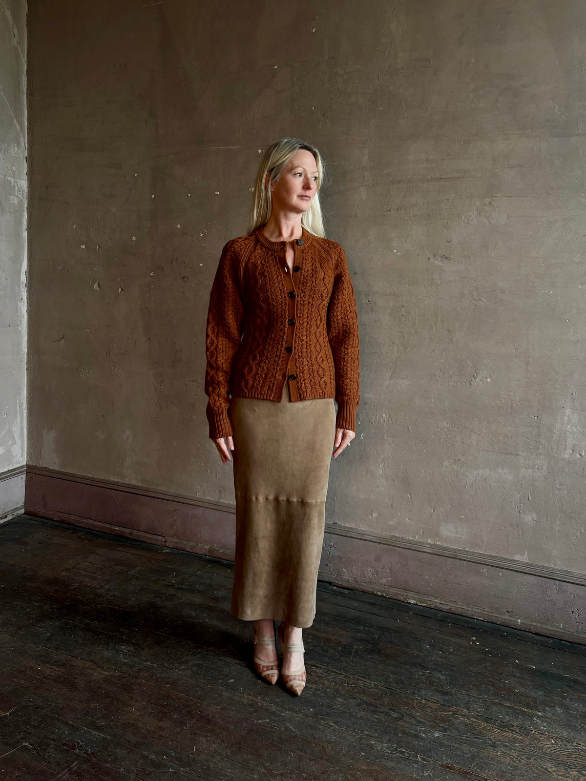 Mature woman wearing Guest in Residence's Cable Sculpted Cardigan Burnt Sienna wool-cashmere cable knit raglan sleeves. Richly textured heirloom-quality warmth