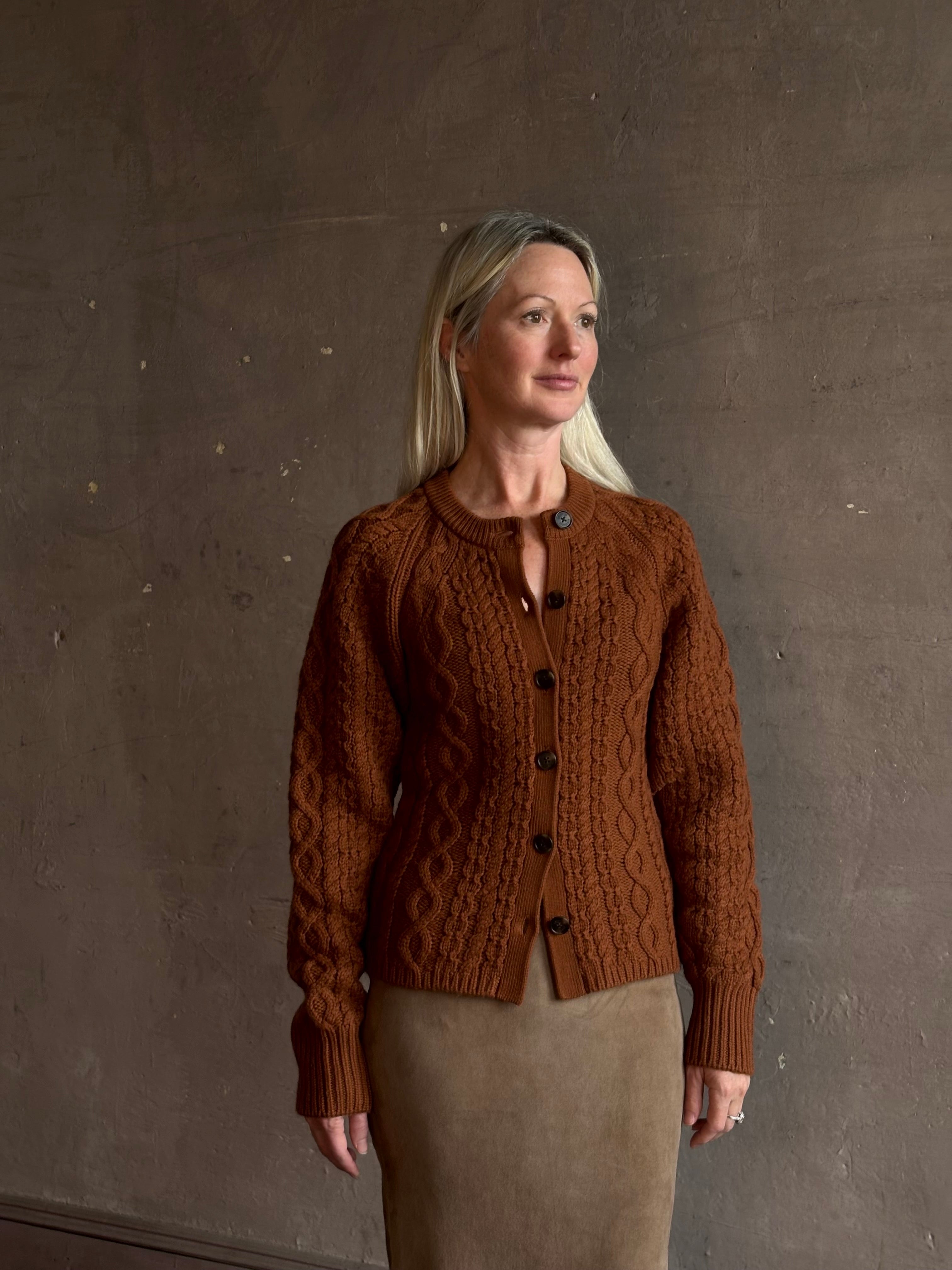 Mature woman wearing Guest in Residence's Cable Sculpted Cardigan Burnt Sienna wool-cashmere cable knit raglan sleeves. Richly textured heirloom-quality warmth