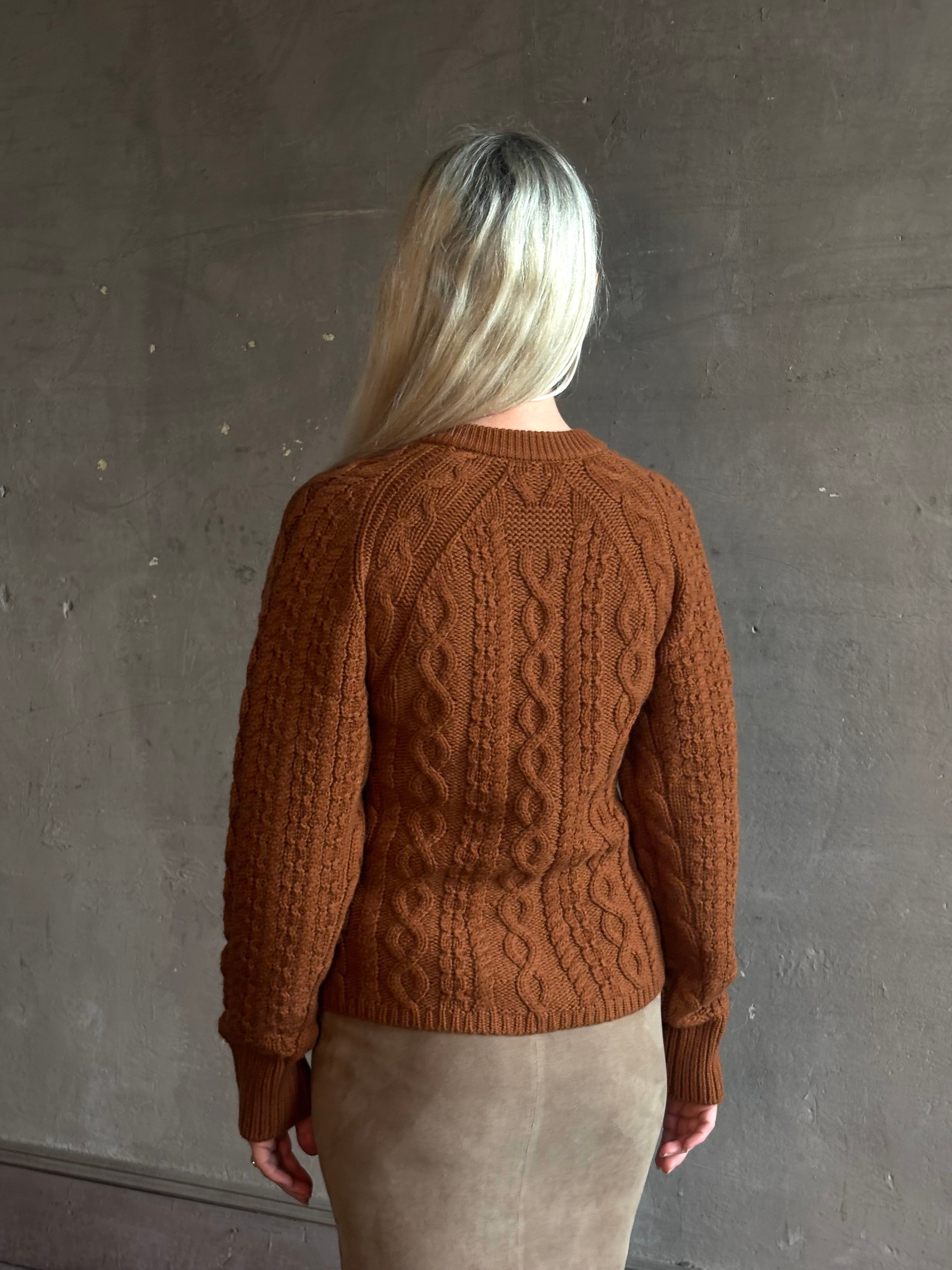 Mature woman wearing Guest in Residence's Cable Sculpted Cardigan Burnt Sienna wool-cashmere cable knit raglan sleeves. Richly textured heirloom-quality warmth