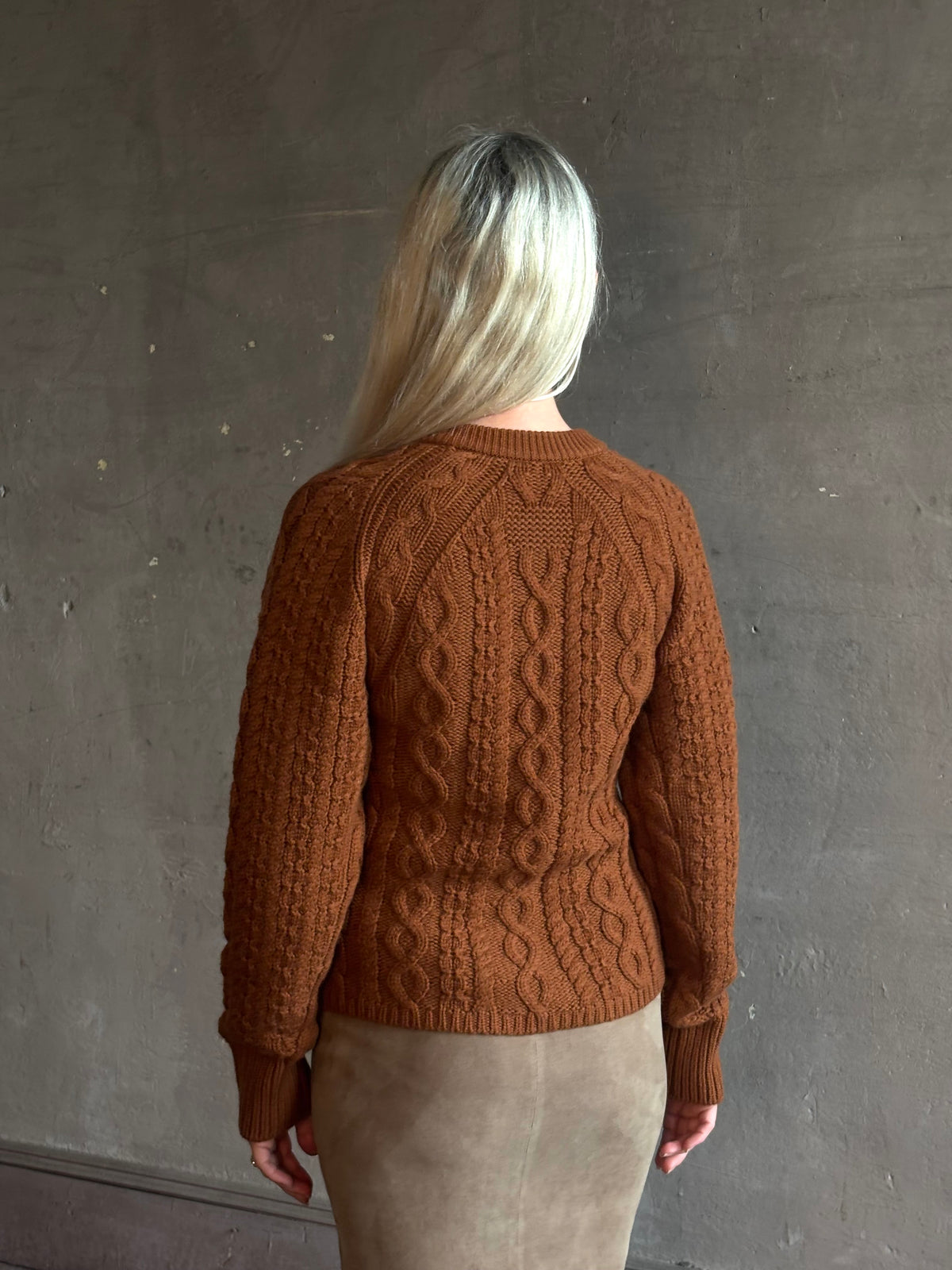 Mature woman wearing Guest in Residence's Cable Sculpted Cardigan Burnt Sienna wool-cashmere cable knit raglan sleeves. Richly textured heirloom-quality warmth