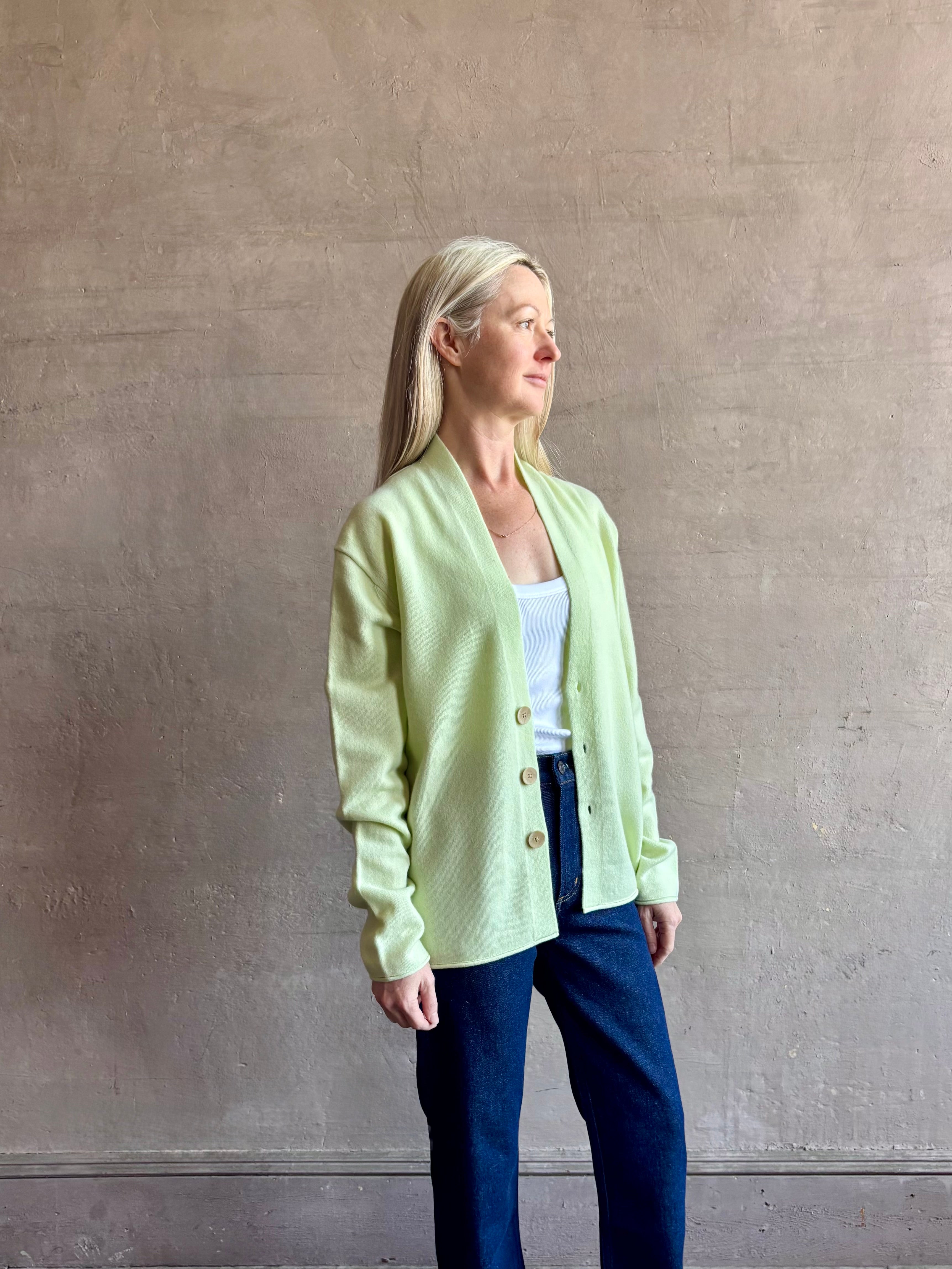 Image of mature woman wearing luxury cashmere sweater GUEST IN RESIDENCE Everywhere Cardigan in Limewash green with long sleeves and three button front v-neck