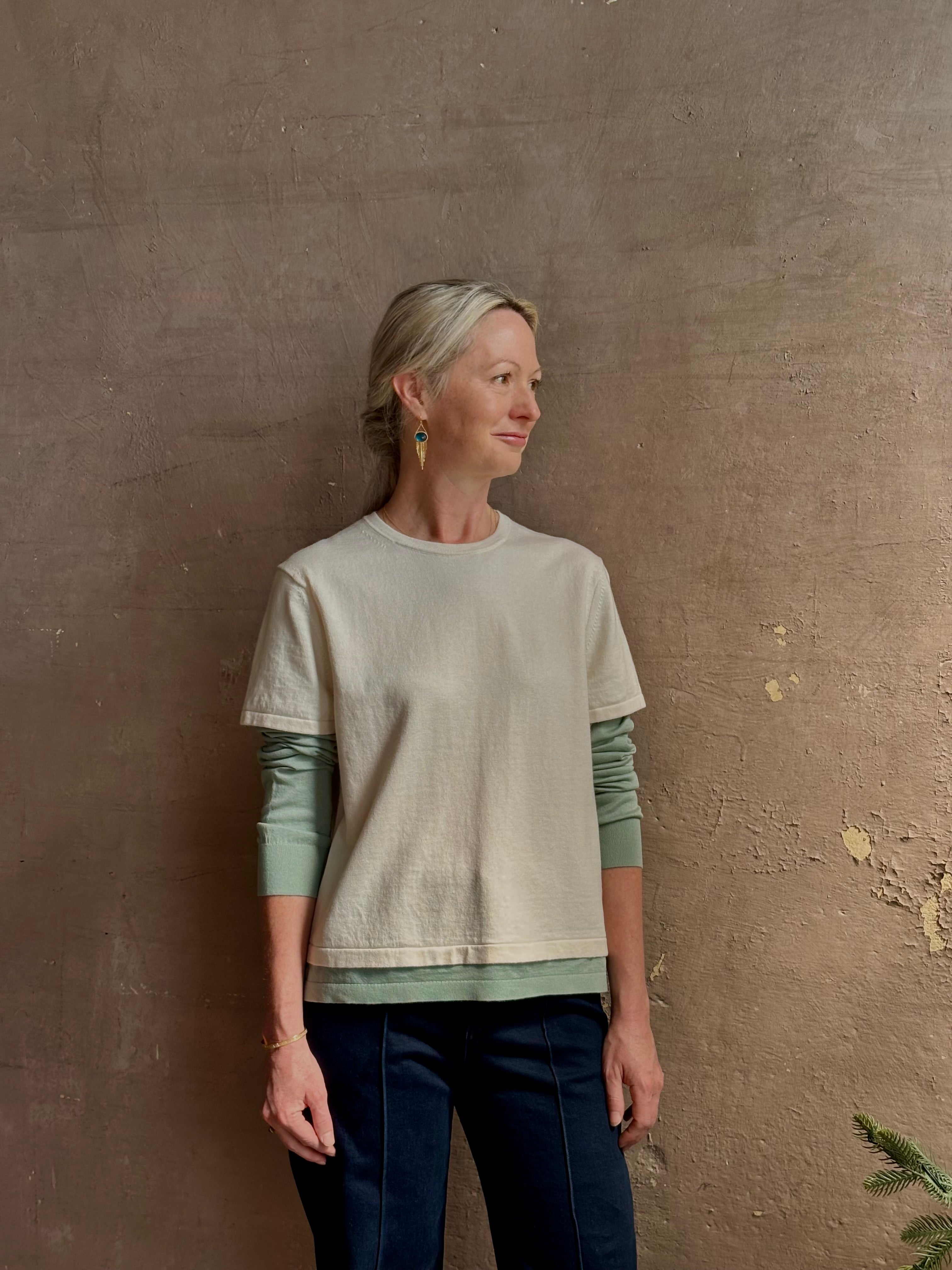 Mature woman wearing elevated luxury Layer Tee Shirt from Guest in Residence rendered in a soft sage brush green and cream colorway and crafted from an exceptional blend of cotton, cashmere, and silk with long sleeves and a crew neckline