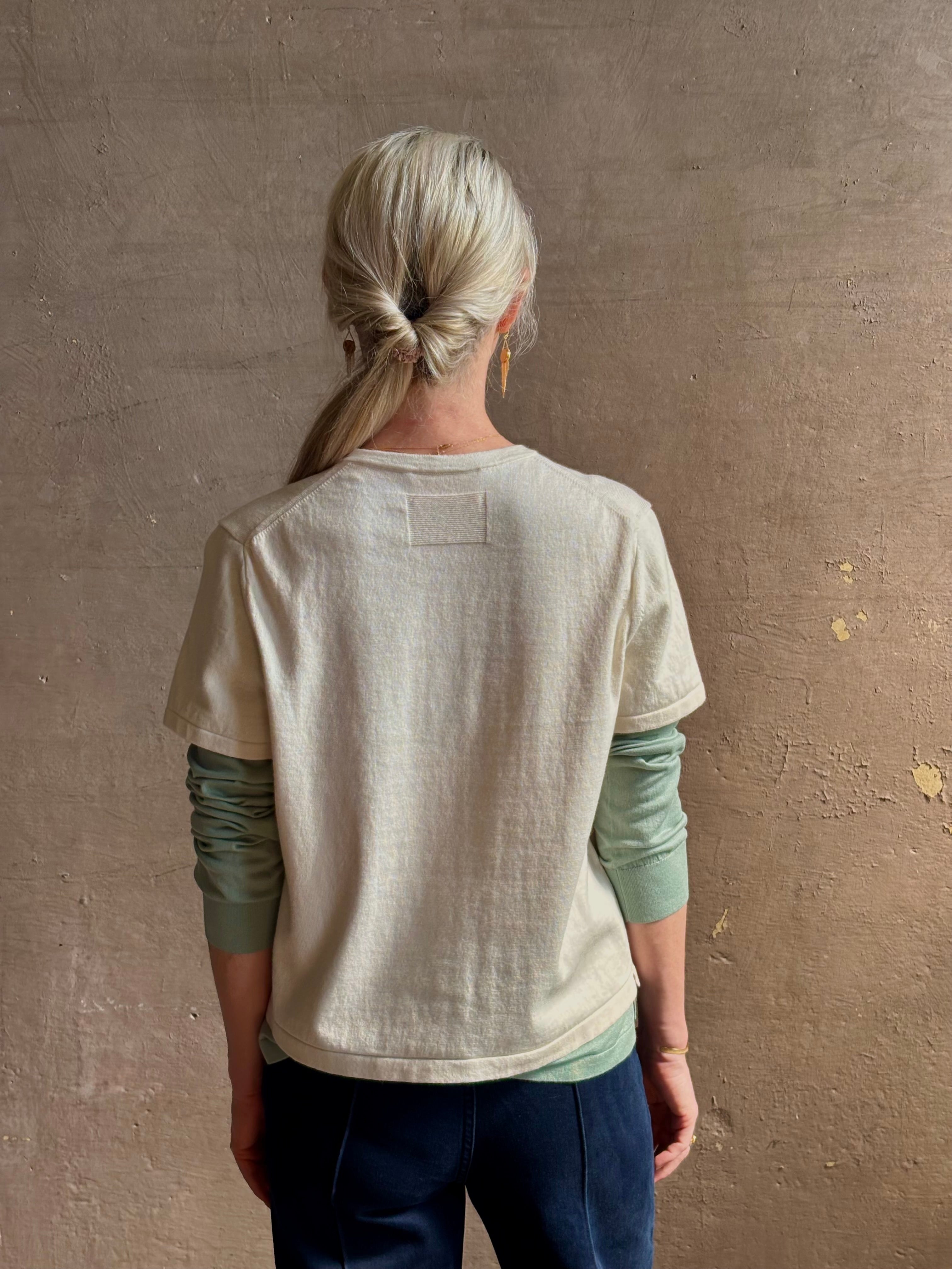 Mature woman wearing elevated luxury Layer Tee Shirt from Guest in Residence rendered in a soft sage brush green and cream colorway and crafted from an exceptional blend of cotton, cashmere, and silk with long sleeves and a crew neckline
