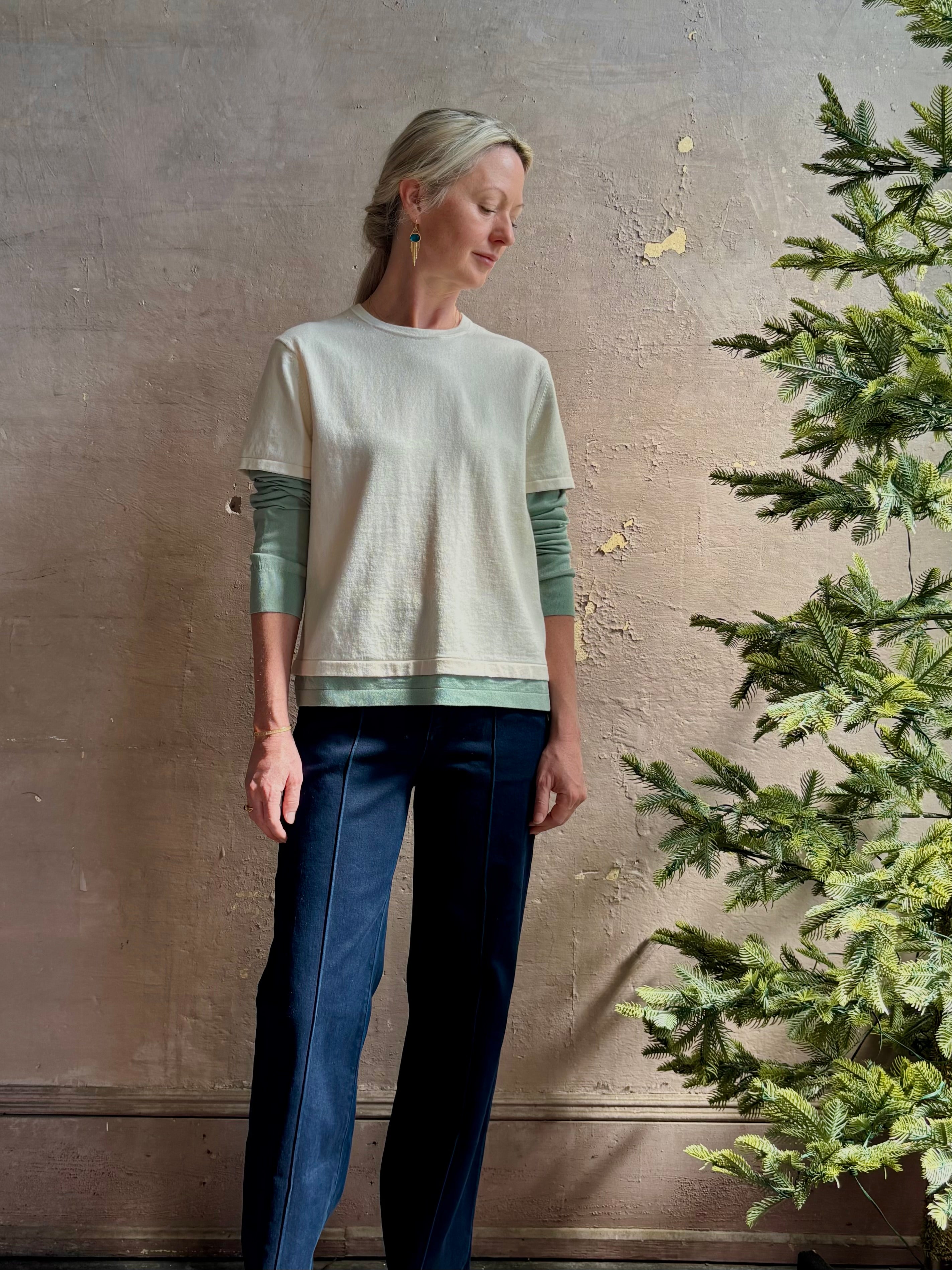 Mature woman wearing elevated luxury Layer Tee Shirt from Guest in Residence rendered in a soft sage brush green and cream colorway and crafted from an exceptional blend of cotton, cashmere, and silk with long sleeves and a crew neckline