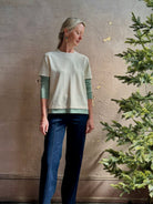 Mature woman wearing elevated luxury Layer Tee Shirt from Guest in Residence rendered in a soft sage brush green and cream colorway and crafted from an exceptional blend of cotton, cashmere, and silk with long sleeves and a crew neckline