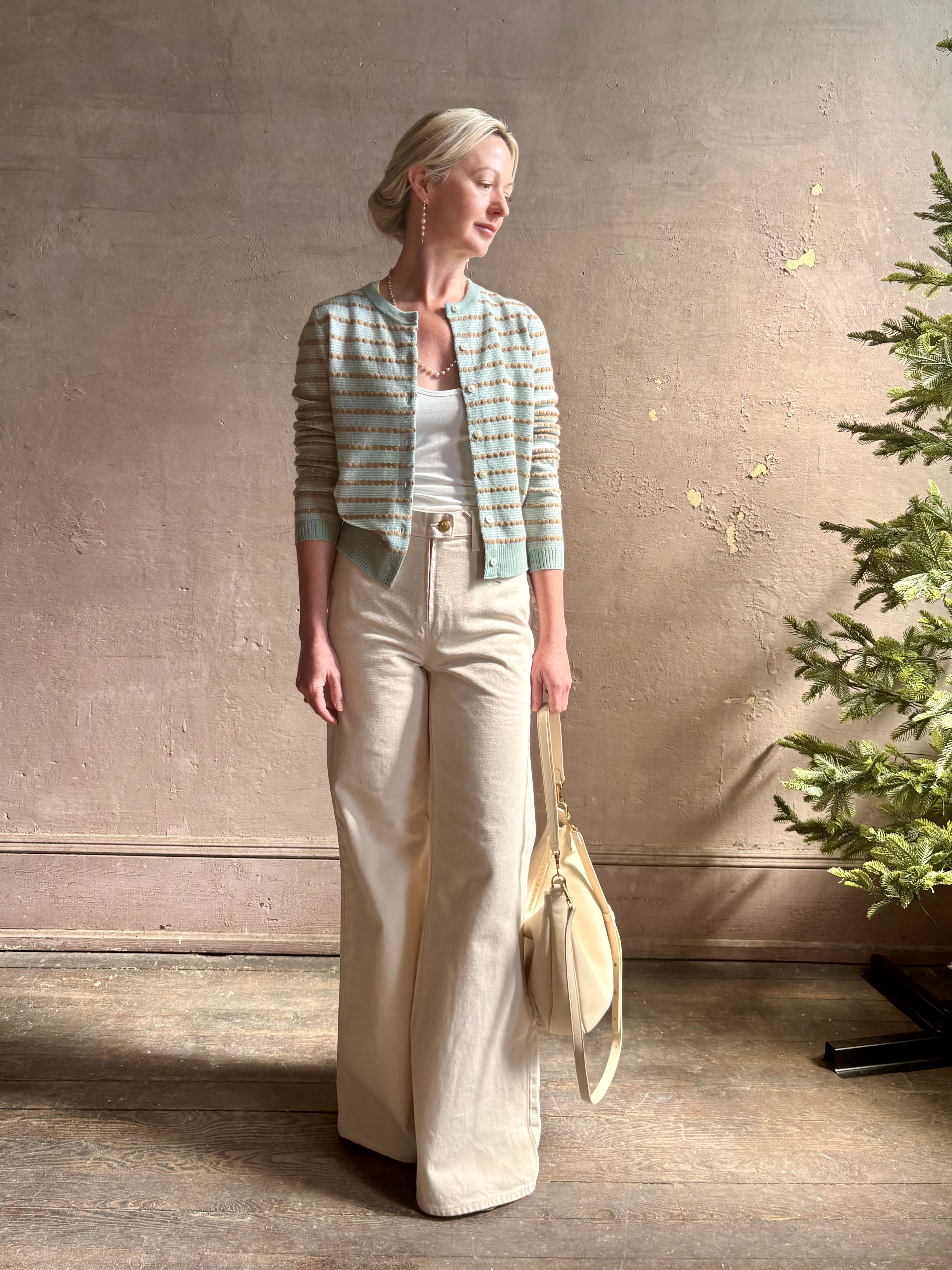 Mature woman wearing Pebble Stripe Jane Cardigan from Guest in Residence rendered in a serene sage brush aqua Khaki combo and crafted from 100% cashmere with crew neck, long sleeves and button front