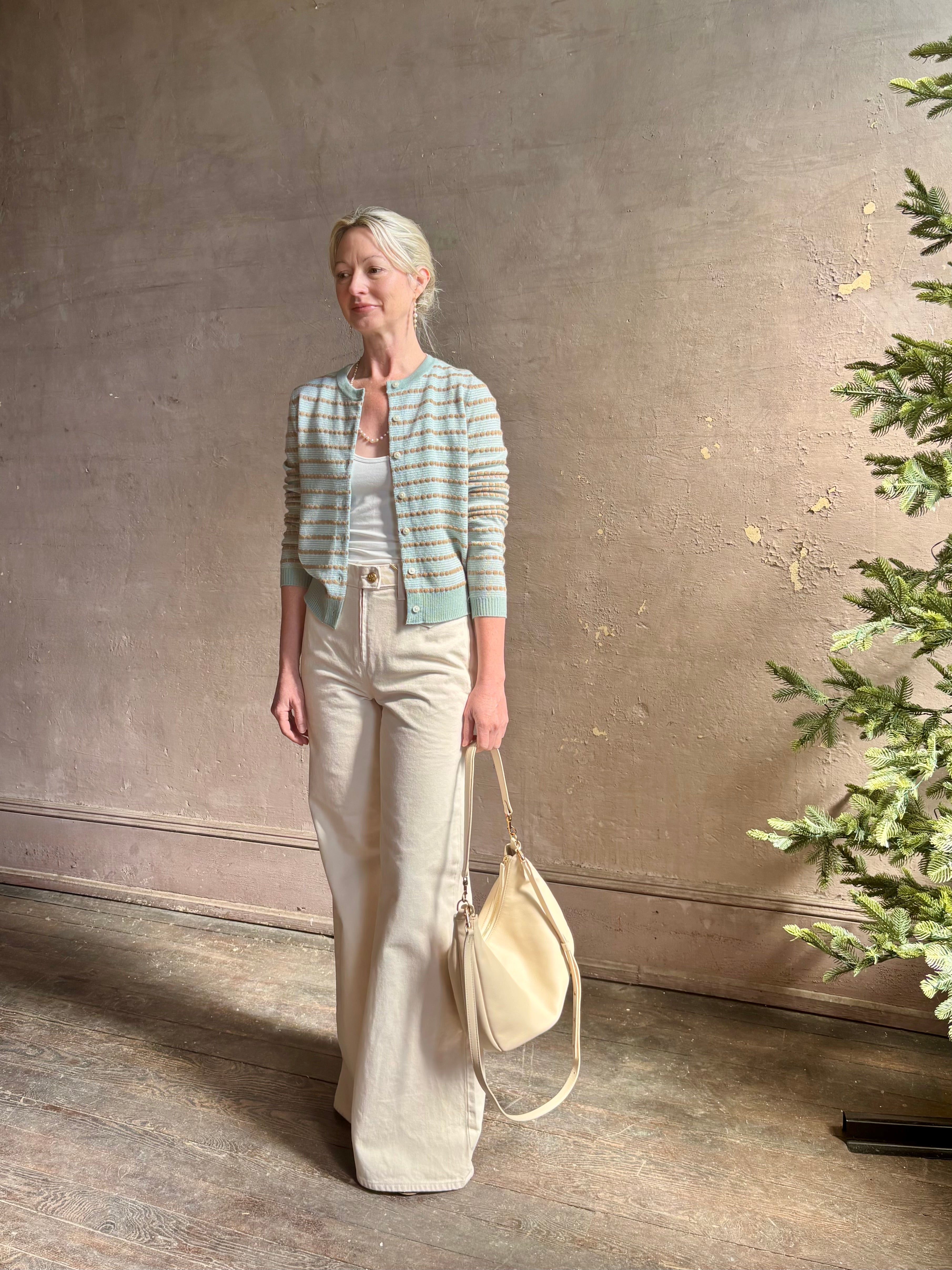 Mature woman wearing Pebble Stripe Jane Cardigan from Guest in Residence rendered in a serene sage brush aqua Khaki combo and crafted from 100% cashmere with crew neck, long sleeves and button front