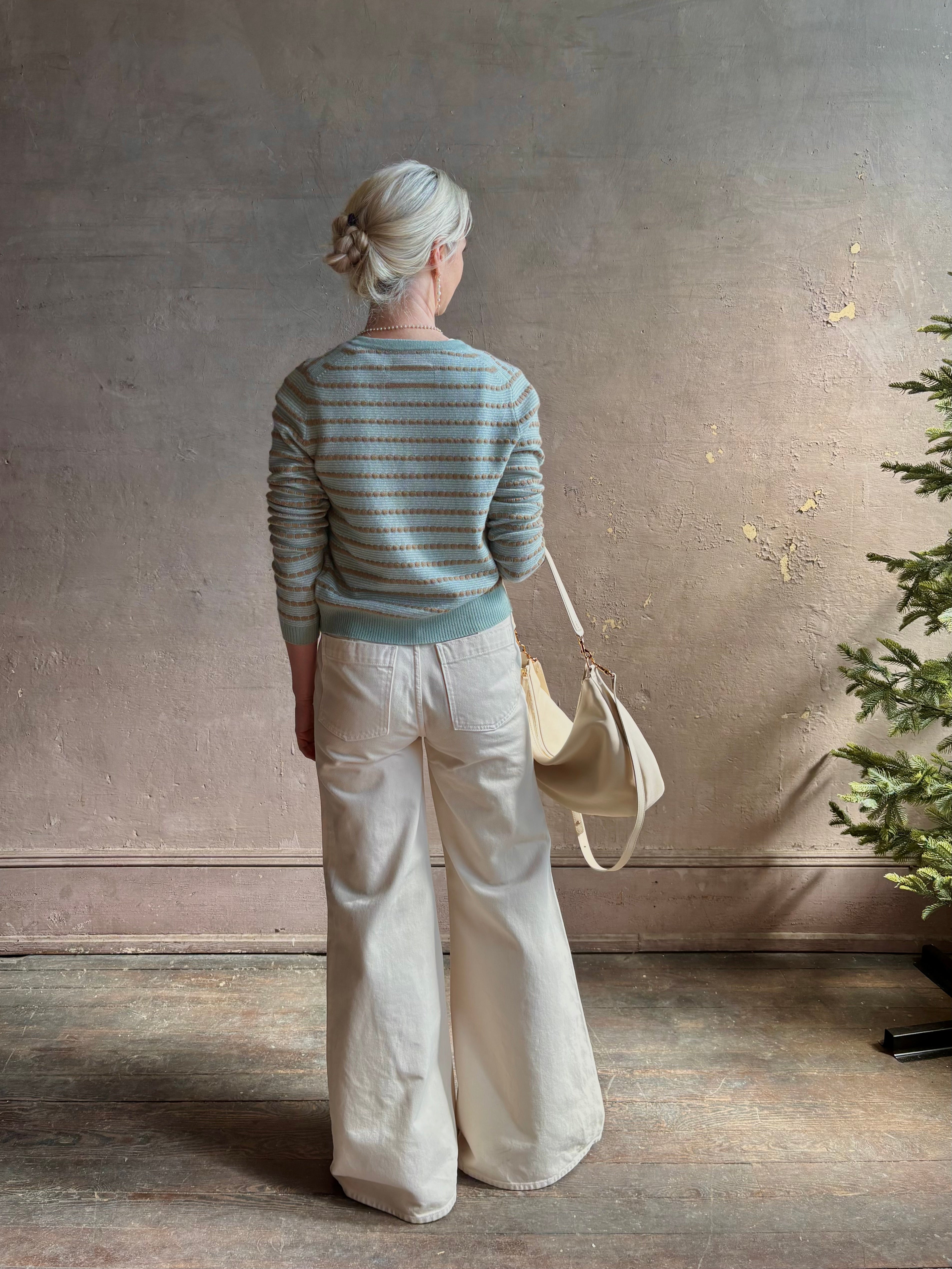 Mature woman wearing Pebble Stripe Jane Cardigan from Guest in Residence rendered in a serene sage brush aqua Khaki combo and crafted from 100% cashmere with crew neck, long sleeves and button front