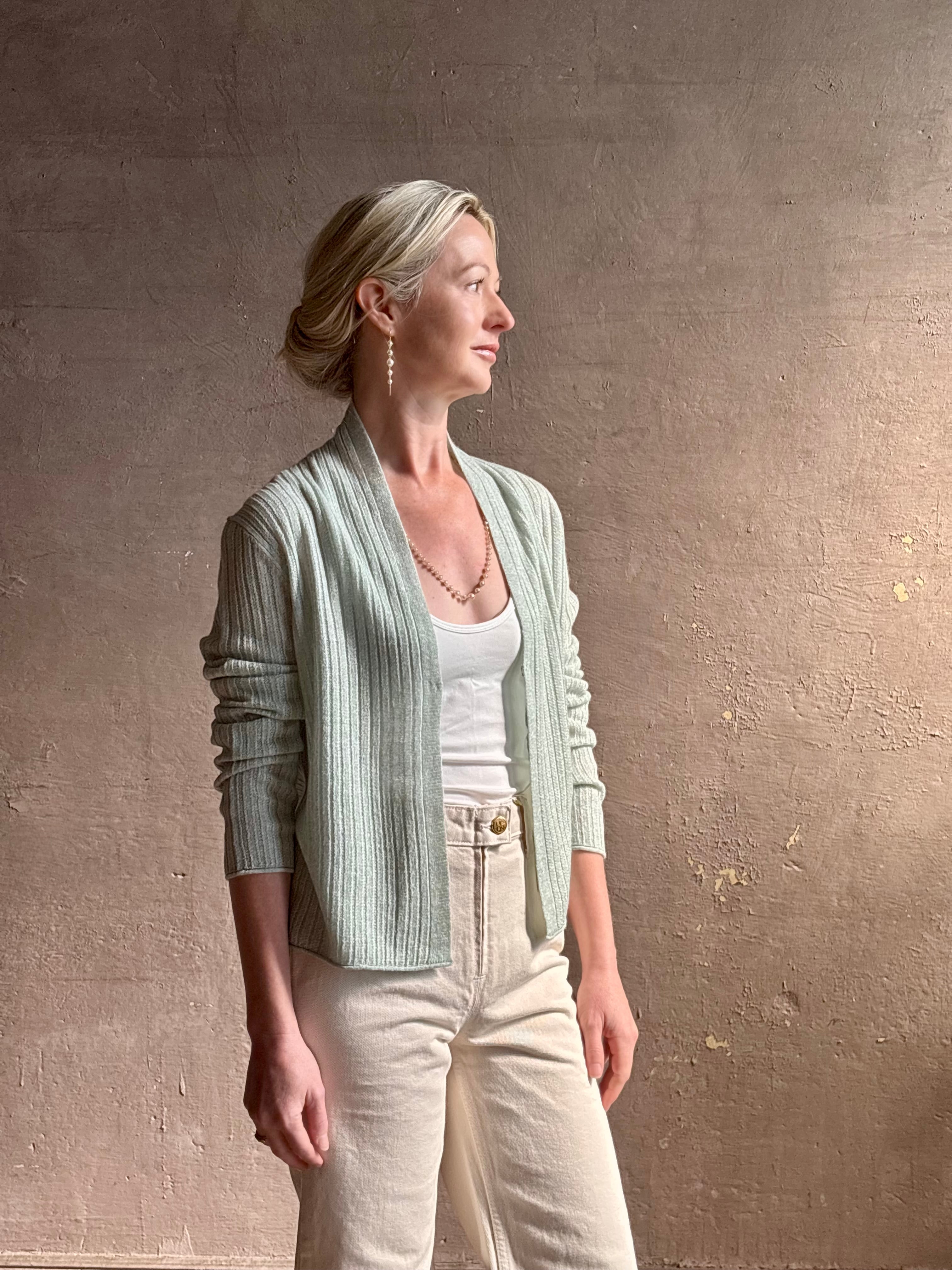 Mature woman wearing Rib Stealth Cardigan from Guest in Residence rendered in a serene sage brush aqua green and crafted from a refined blend of 58% cashmere and 42% linen with long sleeves and a hidden hook and eye closure
