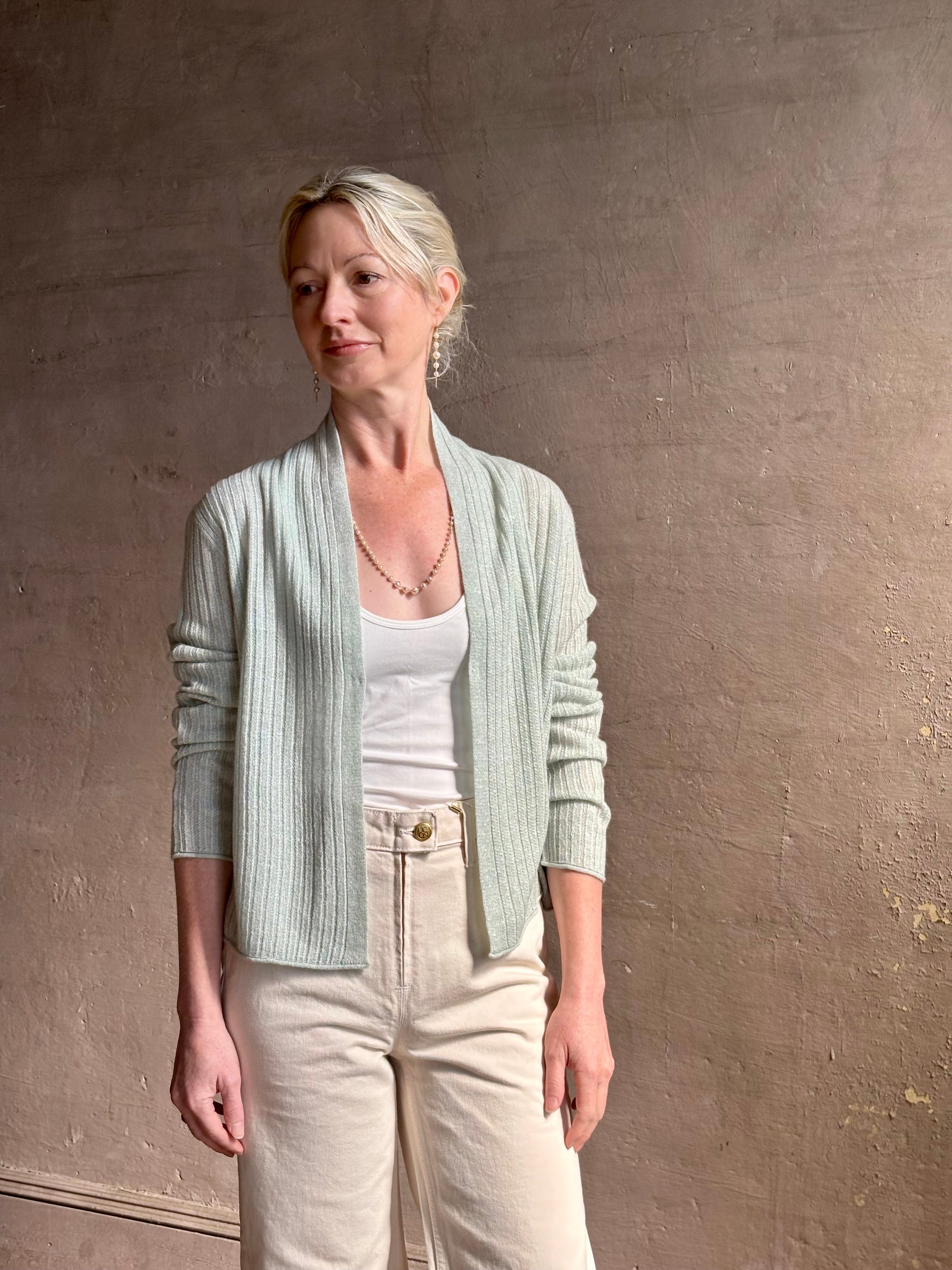 Mature woman wearing Rib Stealth Cardigan from Guest in Residence rendered in a serene sage brush aqua green and crafted from a refined blend of 58% cashmere and 42% linen with long sleeves and a hidden hook and eye closure