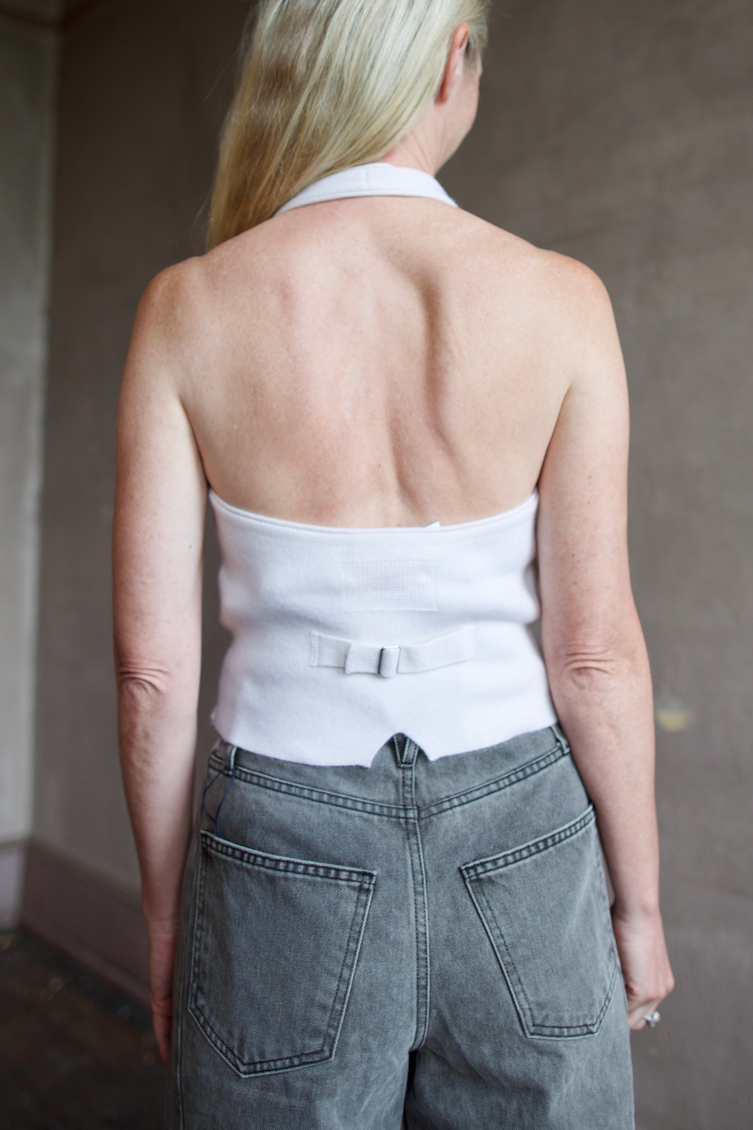 Back of model wearing a white cashmere halter top vest with veronica beard rigid gray denim