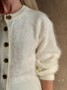 Close up image of Mature woman wearing Guest in Residence’s Grizzly Sculptured Cream brushed cashmere cardigan with henley style long sleeves and contrasting brown buttons
