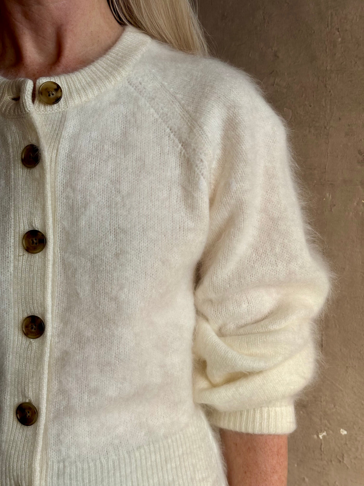 Close up image of Mature woman wearing Guest in Residence’s Grizzly Sculptured Cream brushed cashmere cardigan with henley style long sleeves and contrasting brown buttons