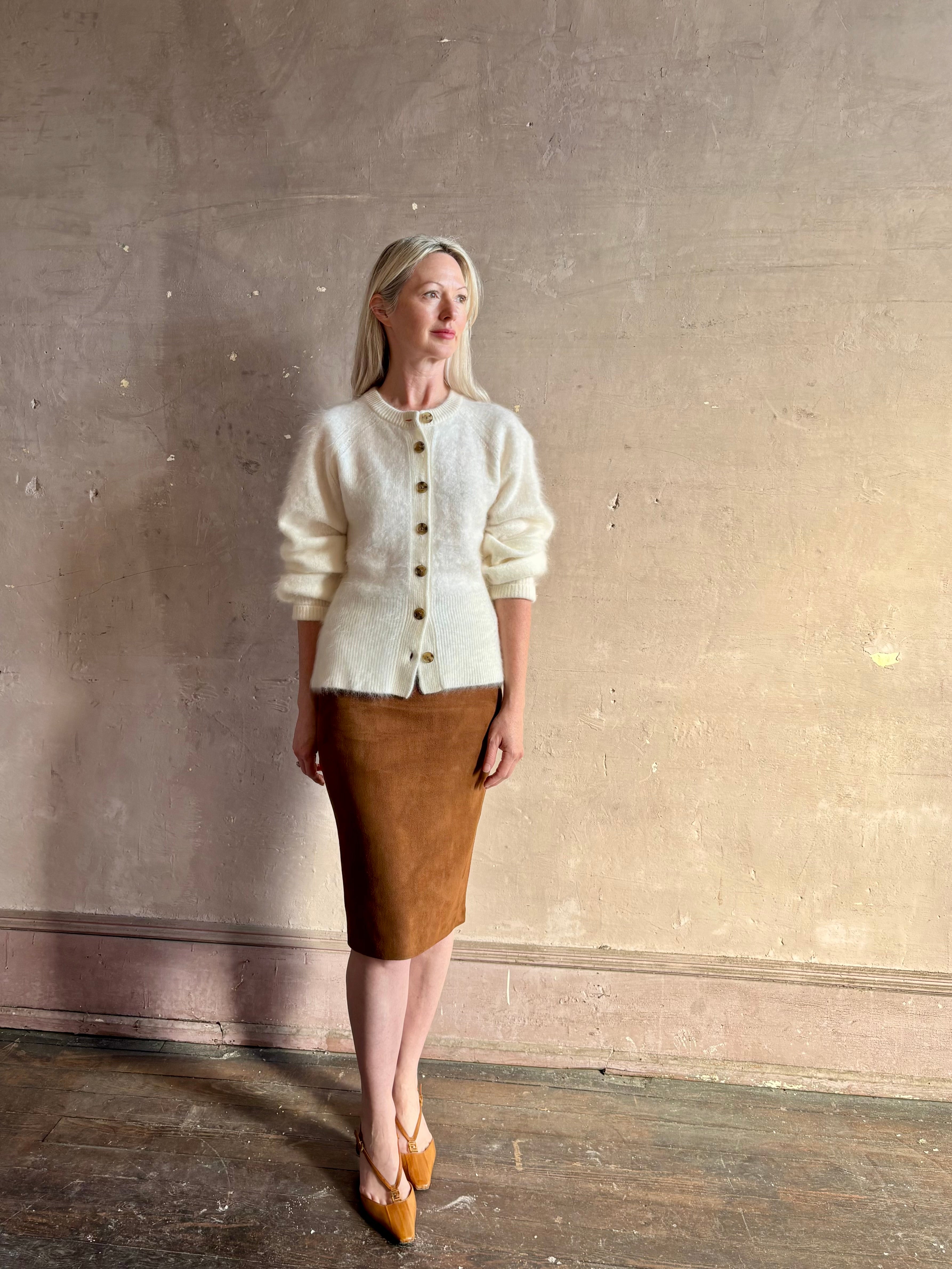 Mature woman wearing a cream-colored brushed cashmere cardigan with brown buttons by Gigi Hadid Guest in Residence  suede leather skirt and Fendi Shoes