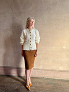 Mature woman wearing a cream-colored brushed cashmere cardigan with brown buttons by Gigi Hadid Guest in Residence  suede leather skirt and Fendi Shoes