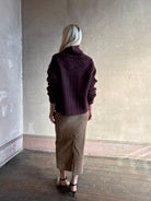 Back image of a woman wearing a dark plum purple cable-knit sweater with intricate pattern all the way around the Guest in Residence turtle neck sweater